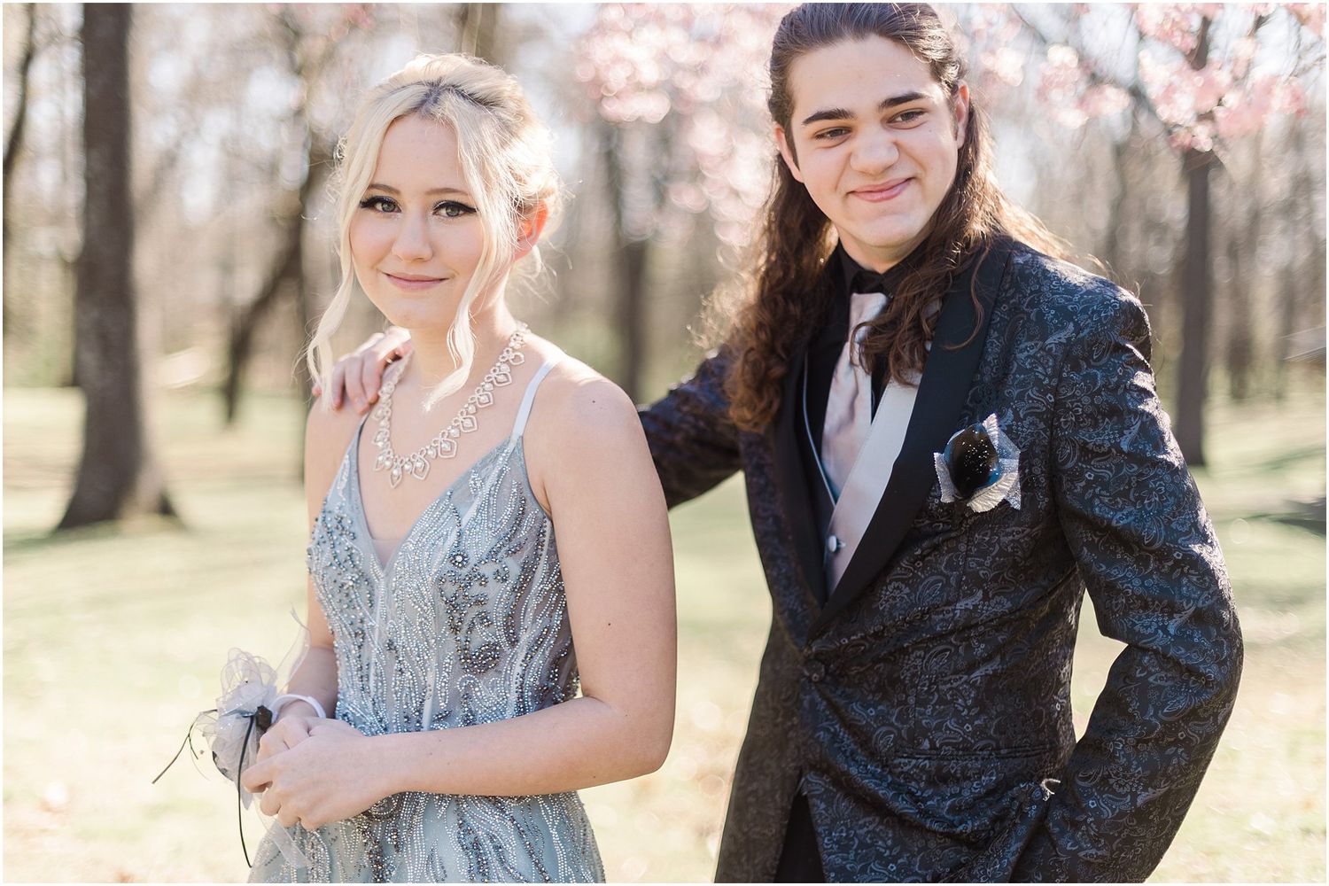 A formal couple poses together outdoors wearing coordinated evening attire.