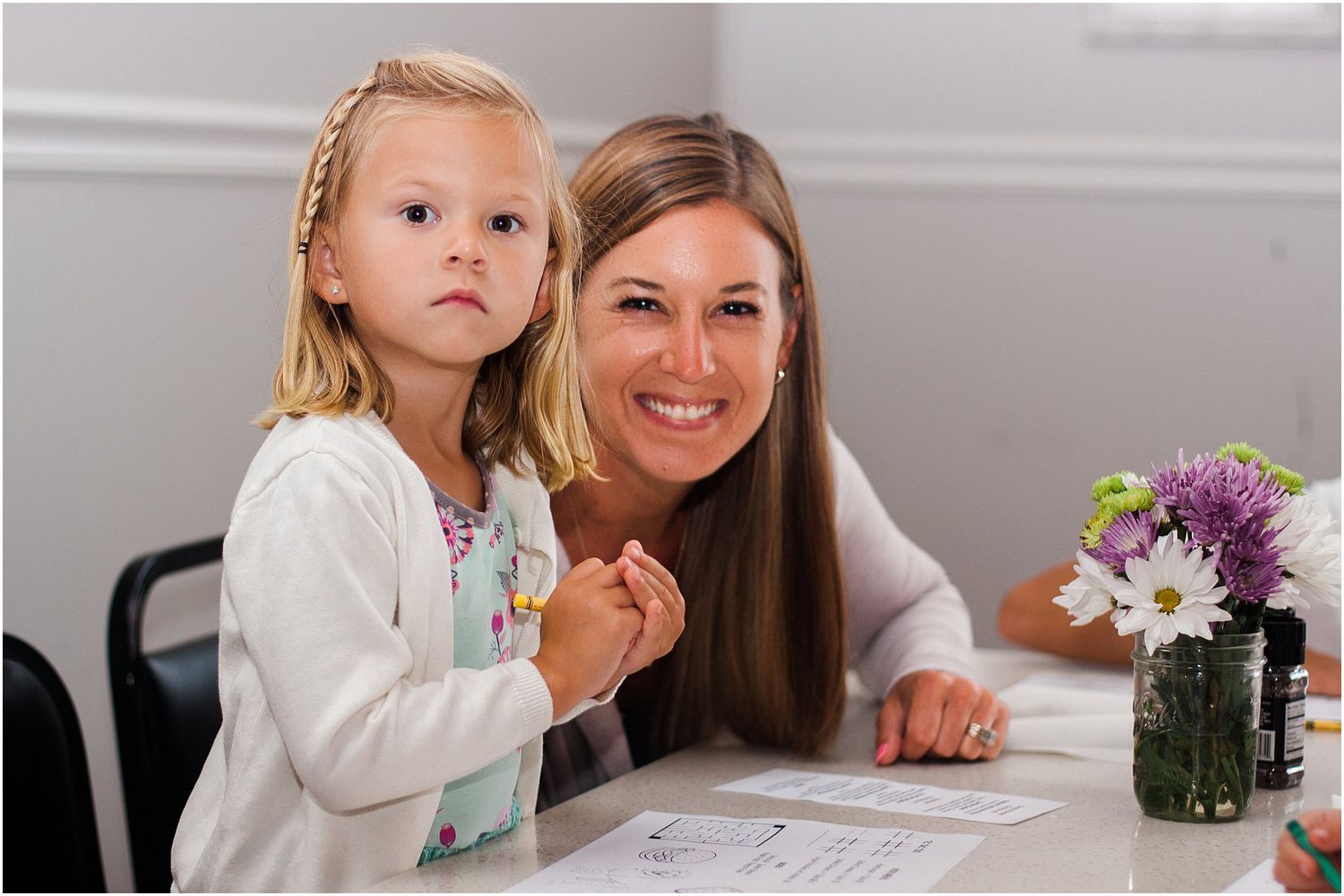 A child and adult sit together at a table looking at papers with flowers nearby.