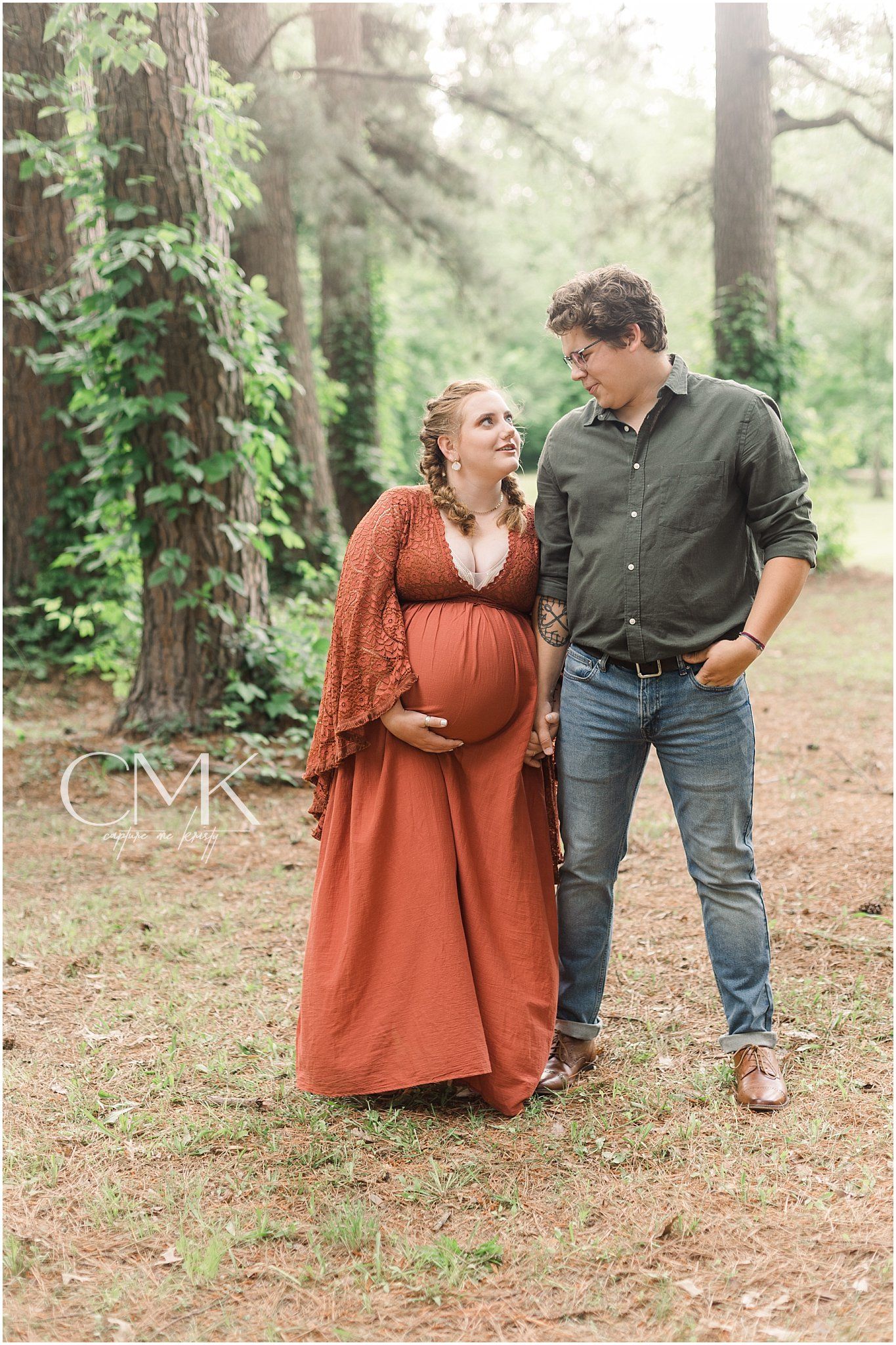 Candid couples maternity photo showing affectionate moment on forest path.