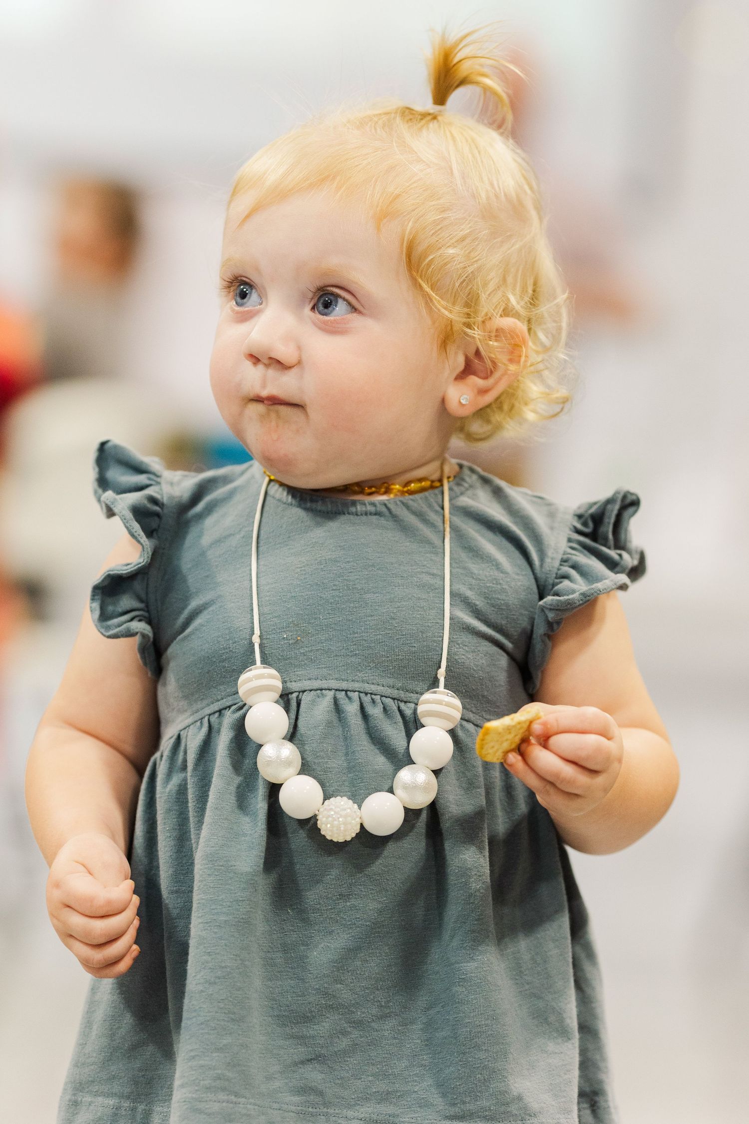Toddler wearing gray dress with white bead necklace looking to the side.