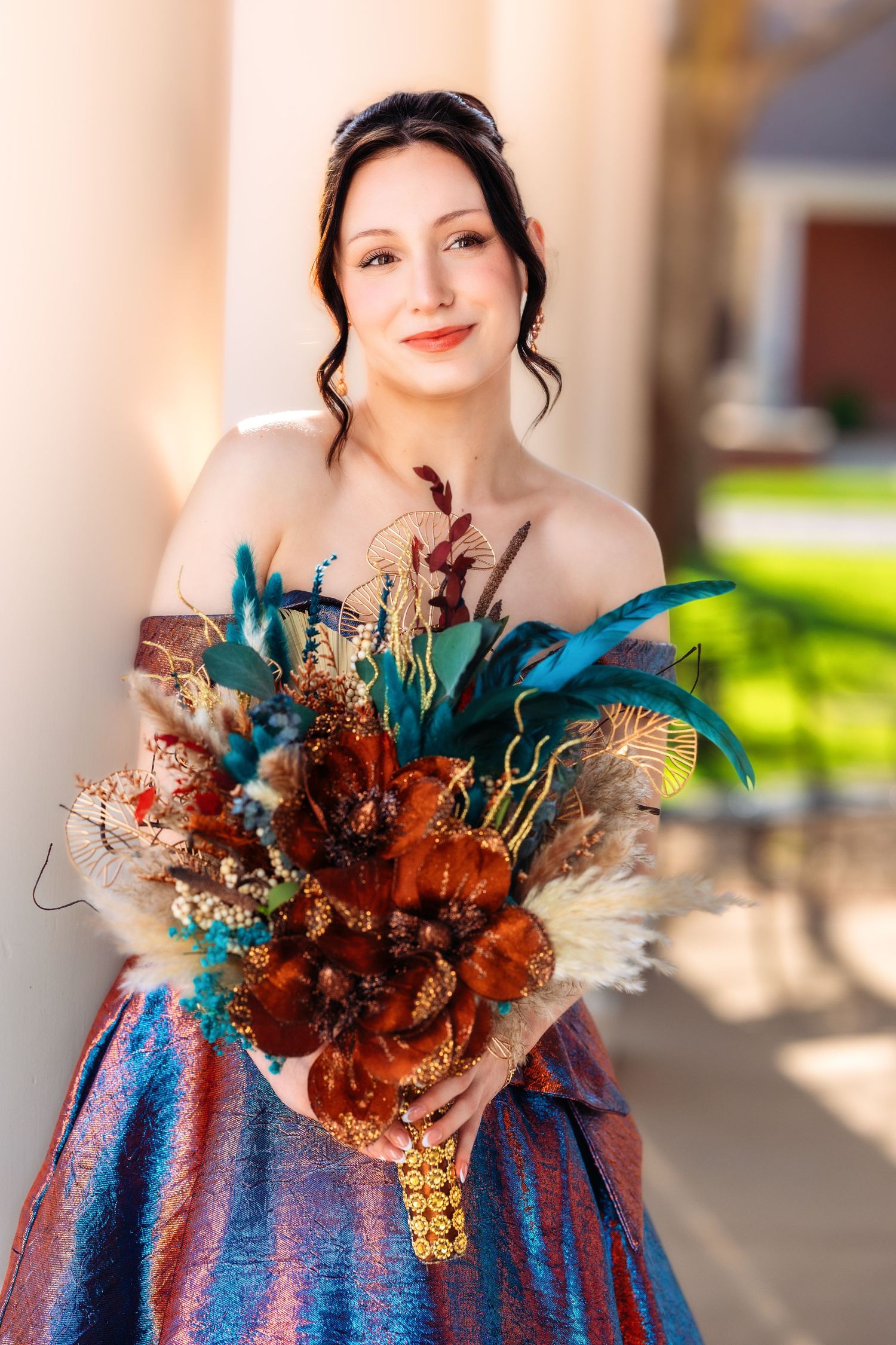 A person wearing a blue and purple dress adorned with a rustic autumn-colored floral arrangement against a light background.