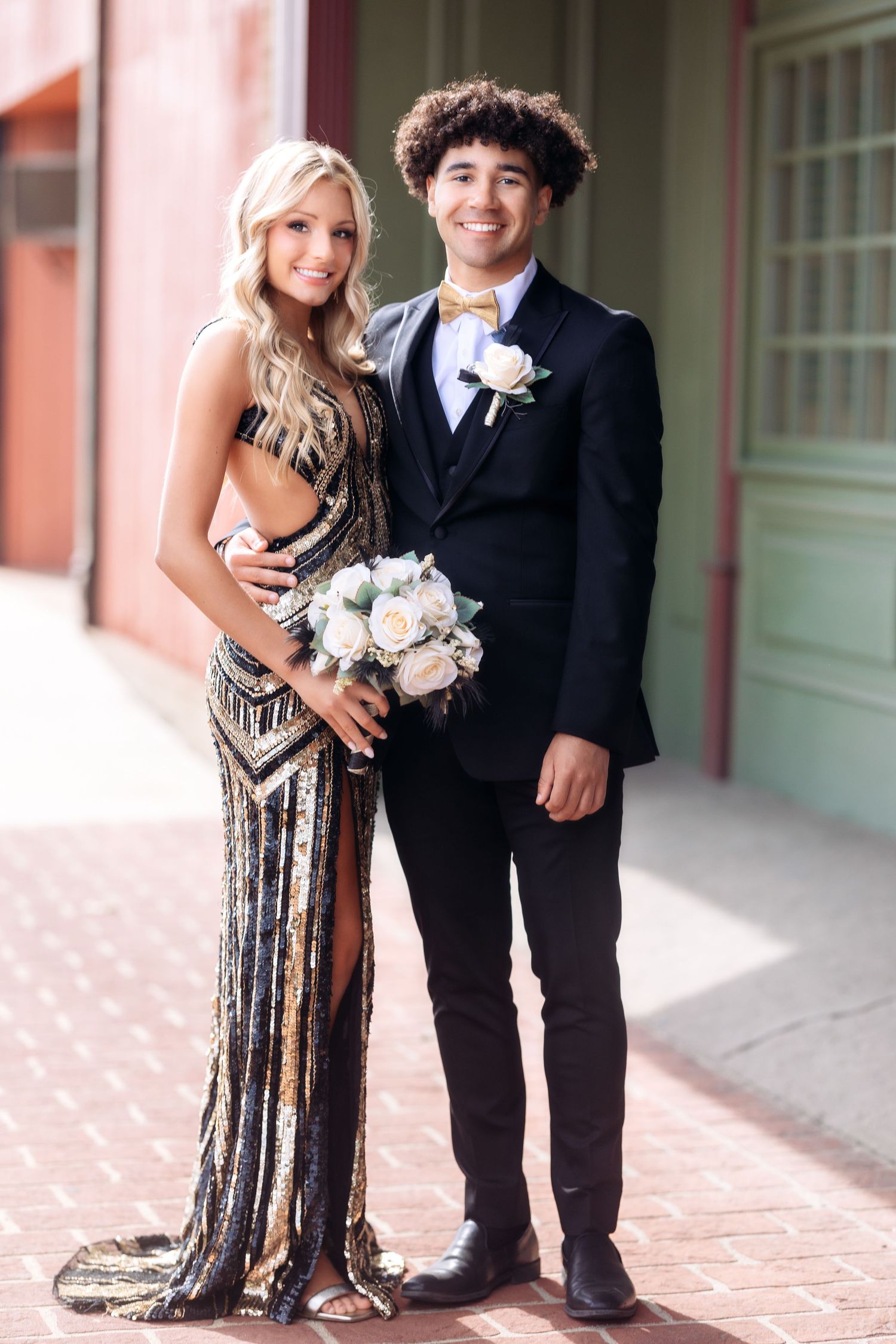 Formal portrait showing sparkly black dress and classic black suit against pink building backdrop.