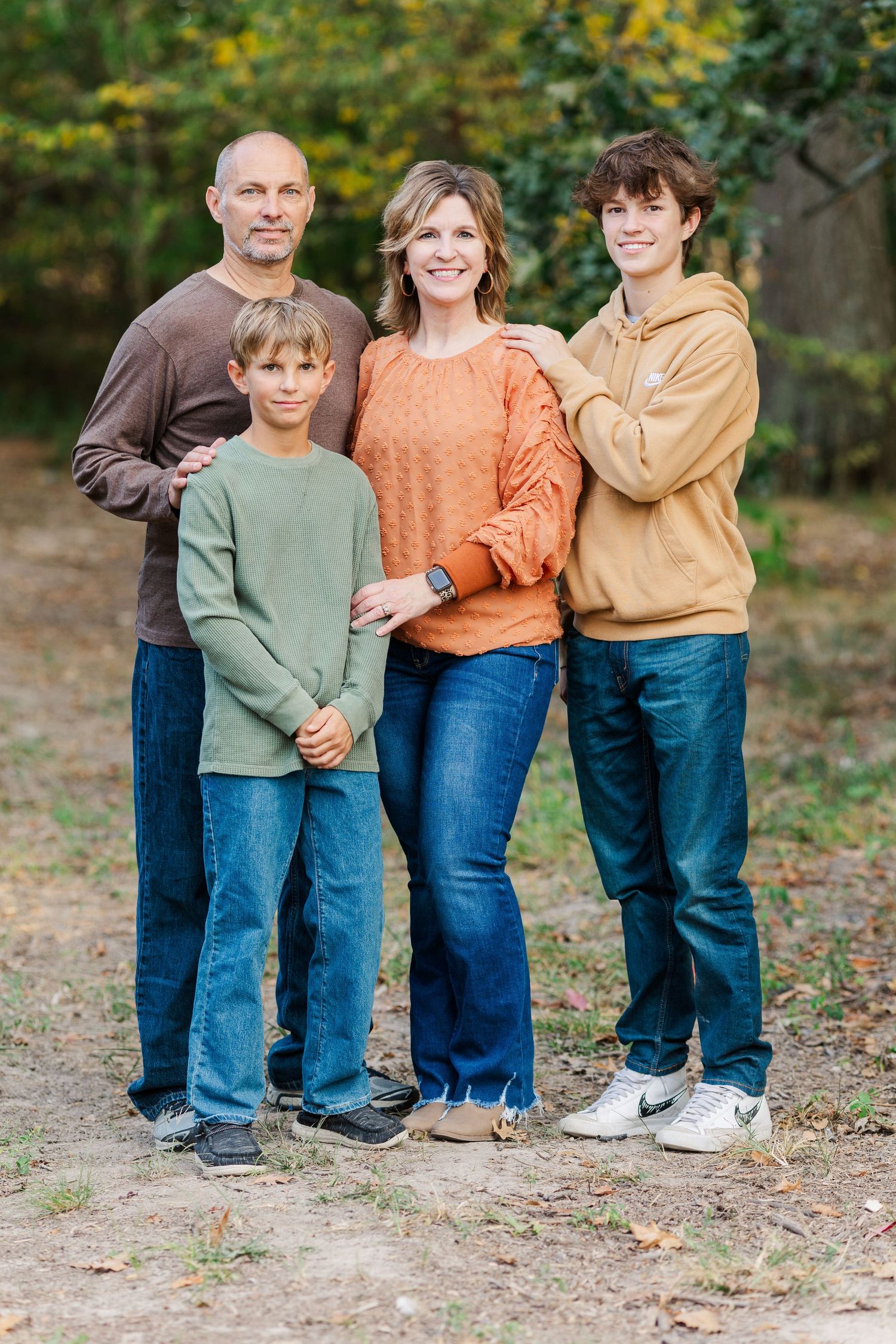 Family group wearing coordinated fall sweaters poses together in a wooded setting.