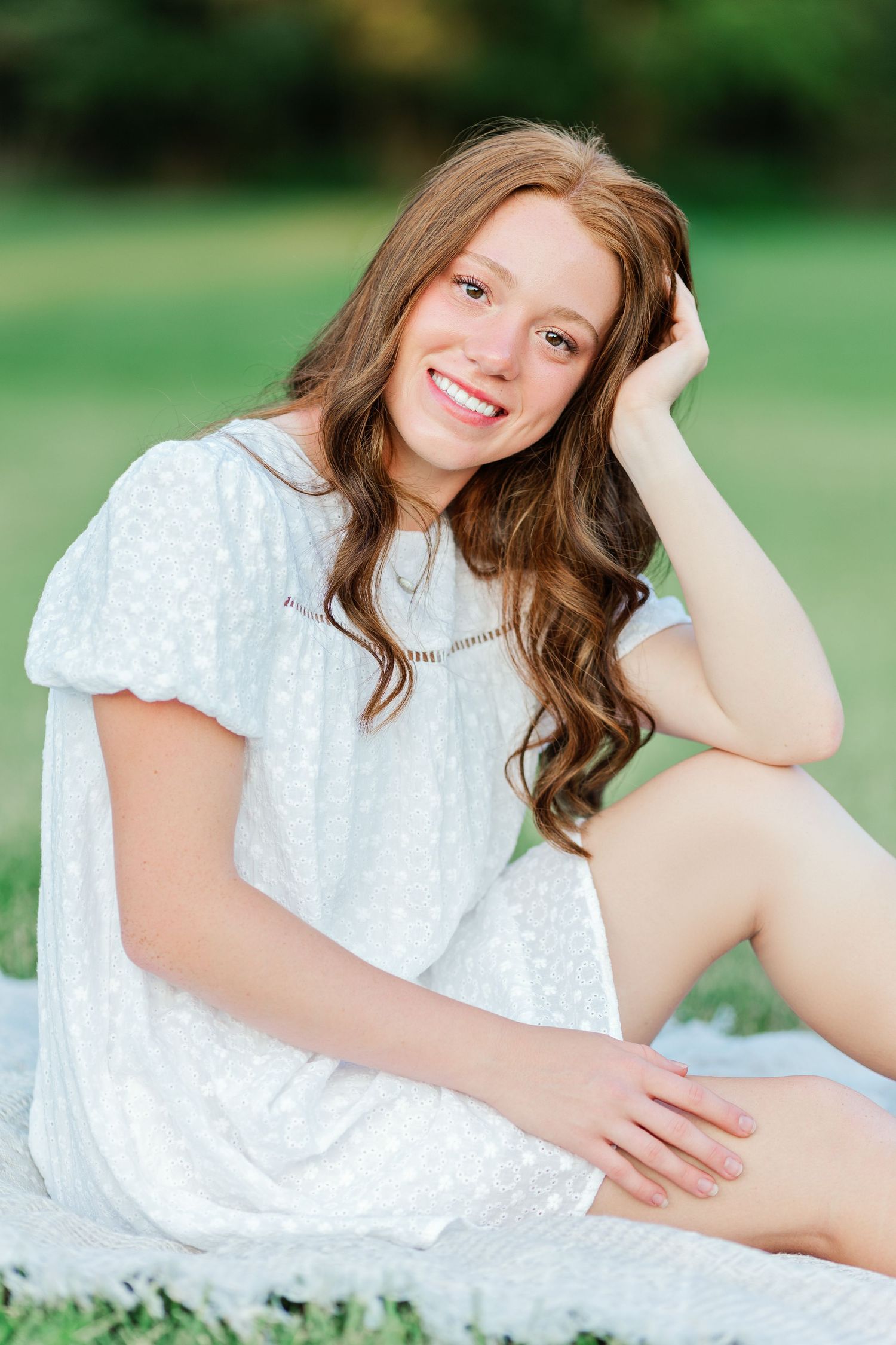 A dreamy summer portrait in a white eyelet dress sitting on grass.