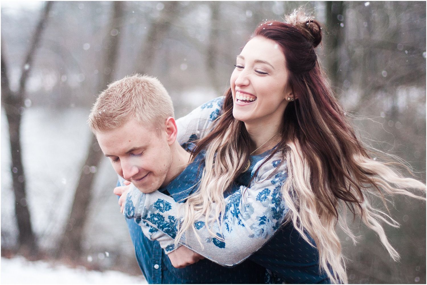 A joyful couple shares laughter during their winter photoshoot with snow falling around them.