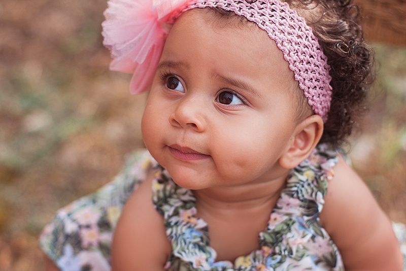Sweet portrait of baby wearing pink headband and floral dress looking to side.