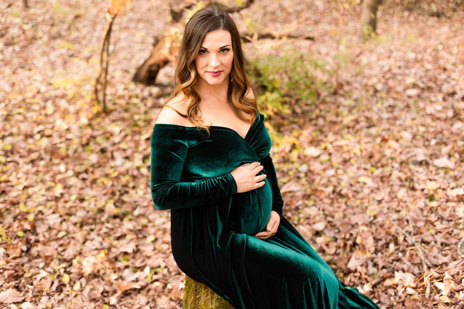 Elegant maternity portrait in forest setting with flowing emerald velvet dress.