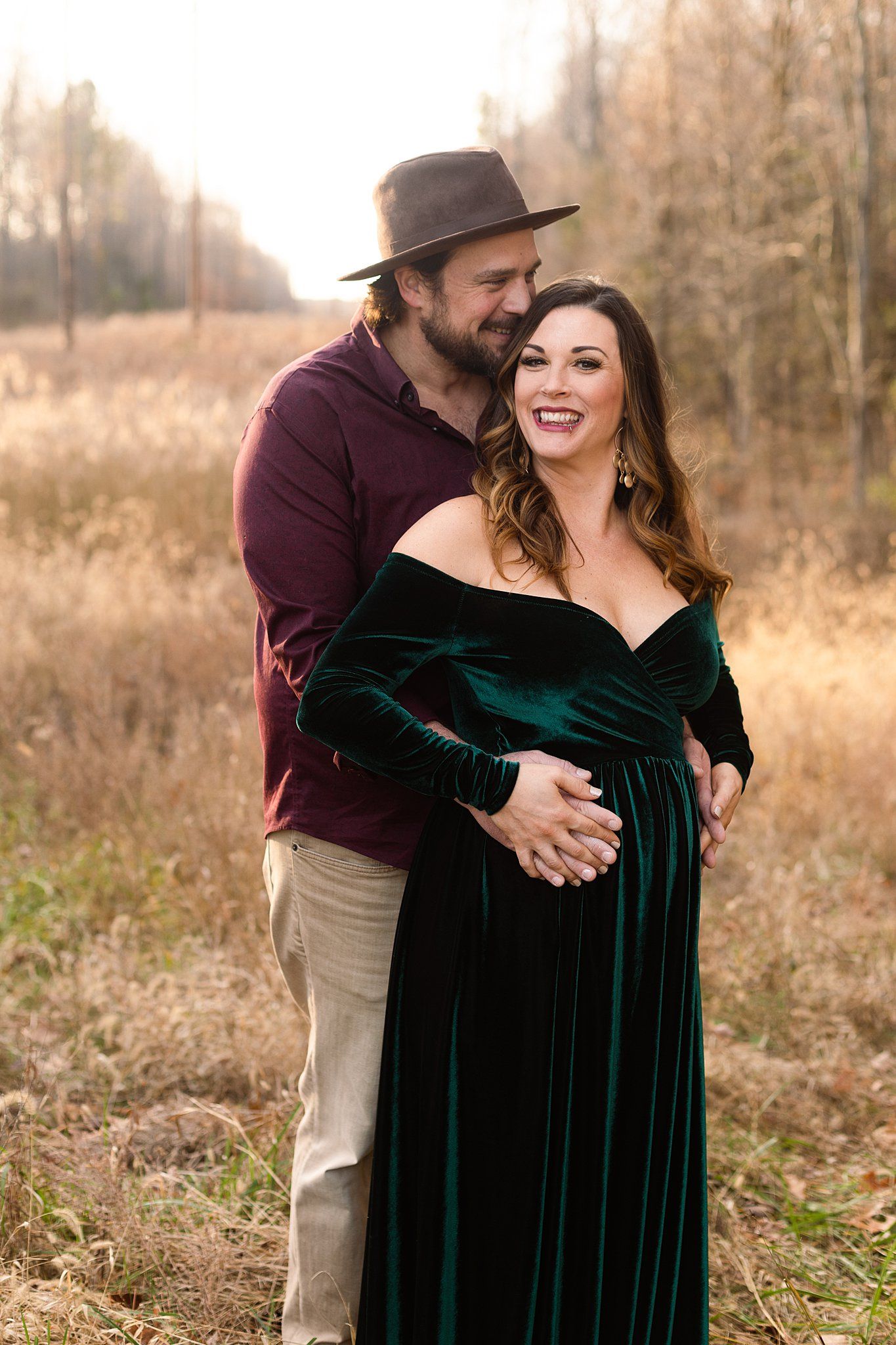 Couple shares intimate moment during maternity shoot wearing velvet dress and fedora.