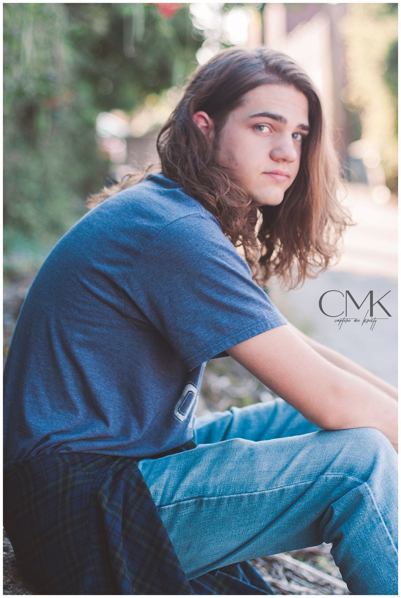 A casual portrait of someone with long hair wearing a blue t-shirt and jeans outdoors.