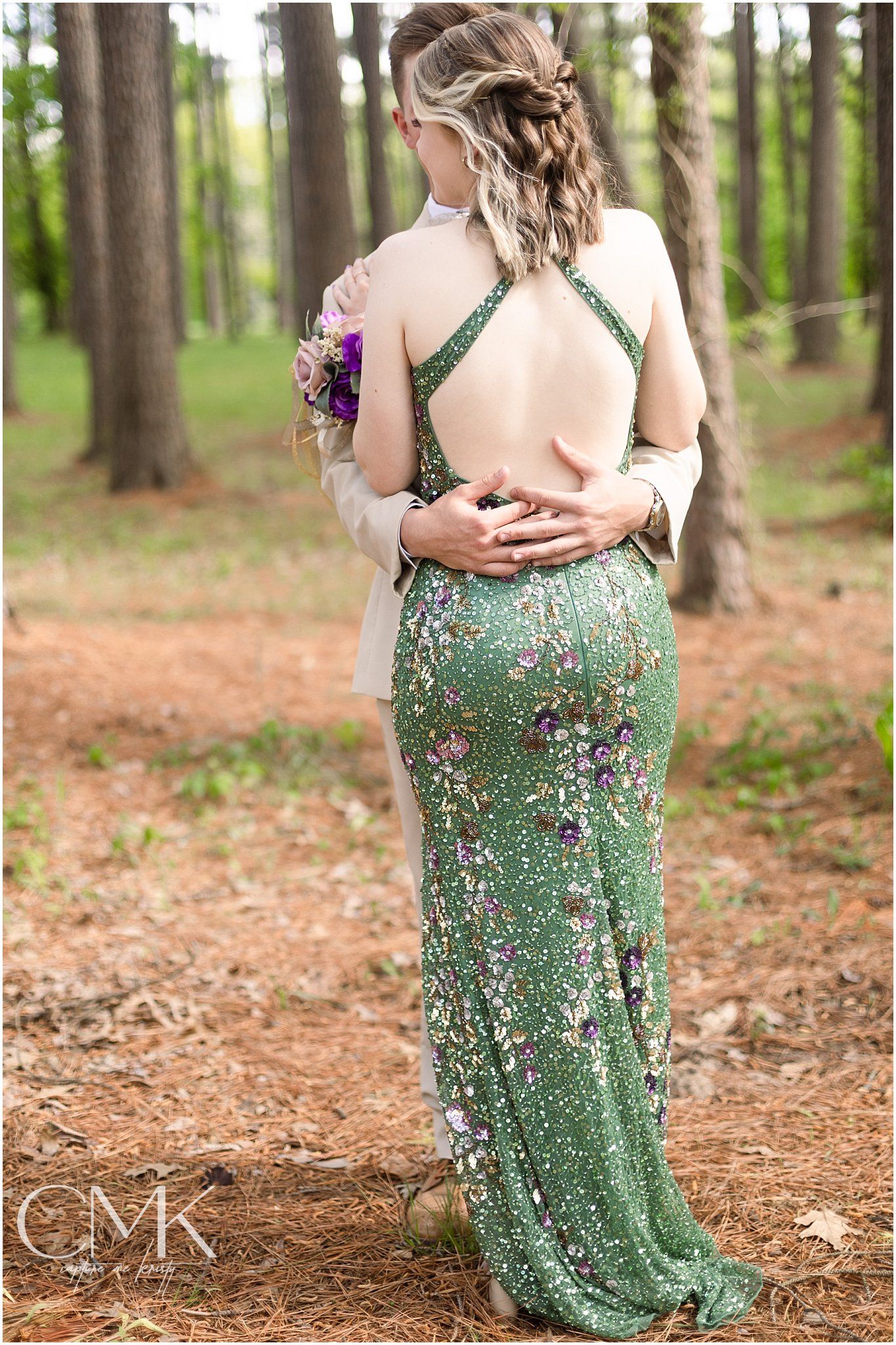 Couple embracing in a forest wearing formal attire with a sparkly green dress and corsage.