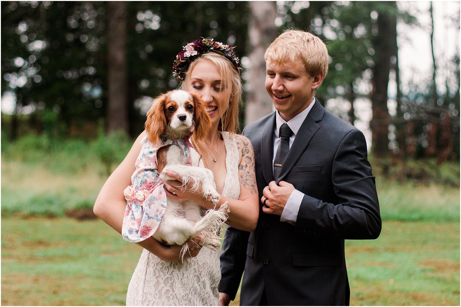 Bride and groom share joyful moment with their Cavalier King Charles Spaniel in the woods.