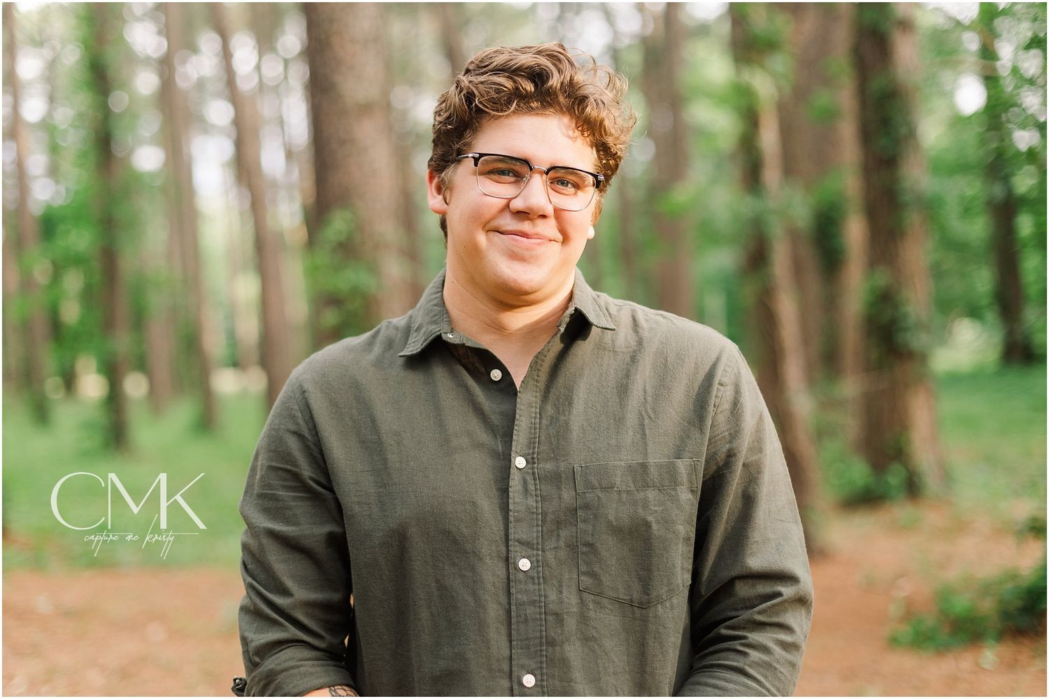 Portrait in a forest setting wearing a gray button-down shirt.