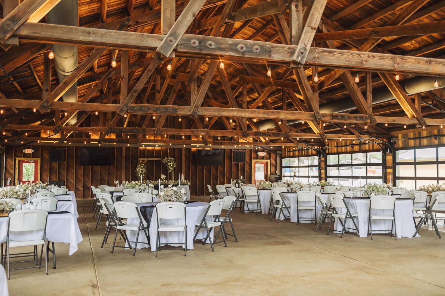 Rustic wooden barn interior set up for a wedding reception with white chairs and tables under exposed beams.