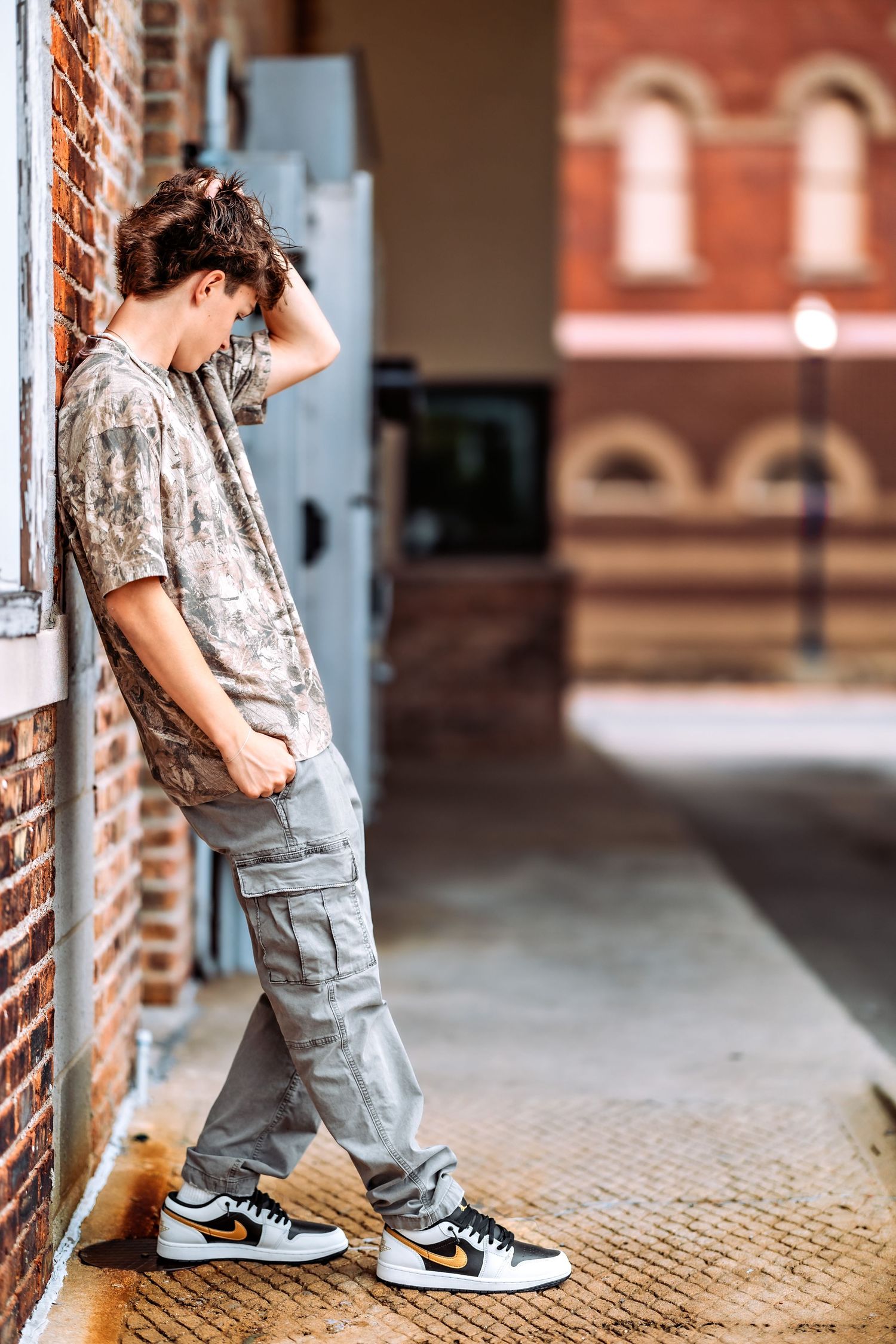 Person in casual attire with cargo pants and sneakers leans against brick wall near vintage building entrance.