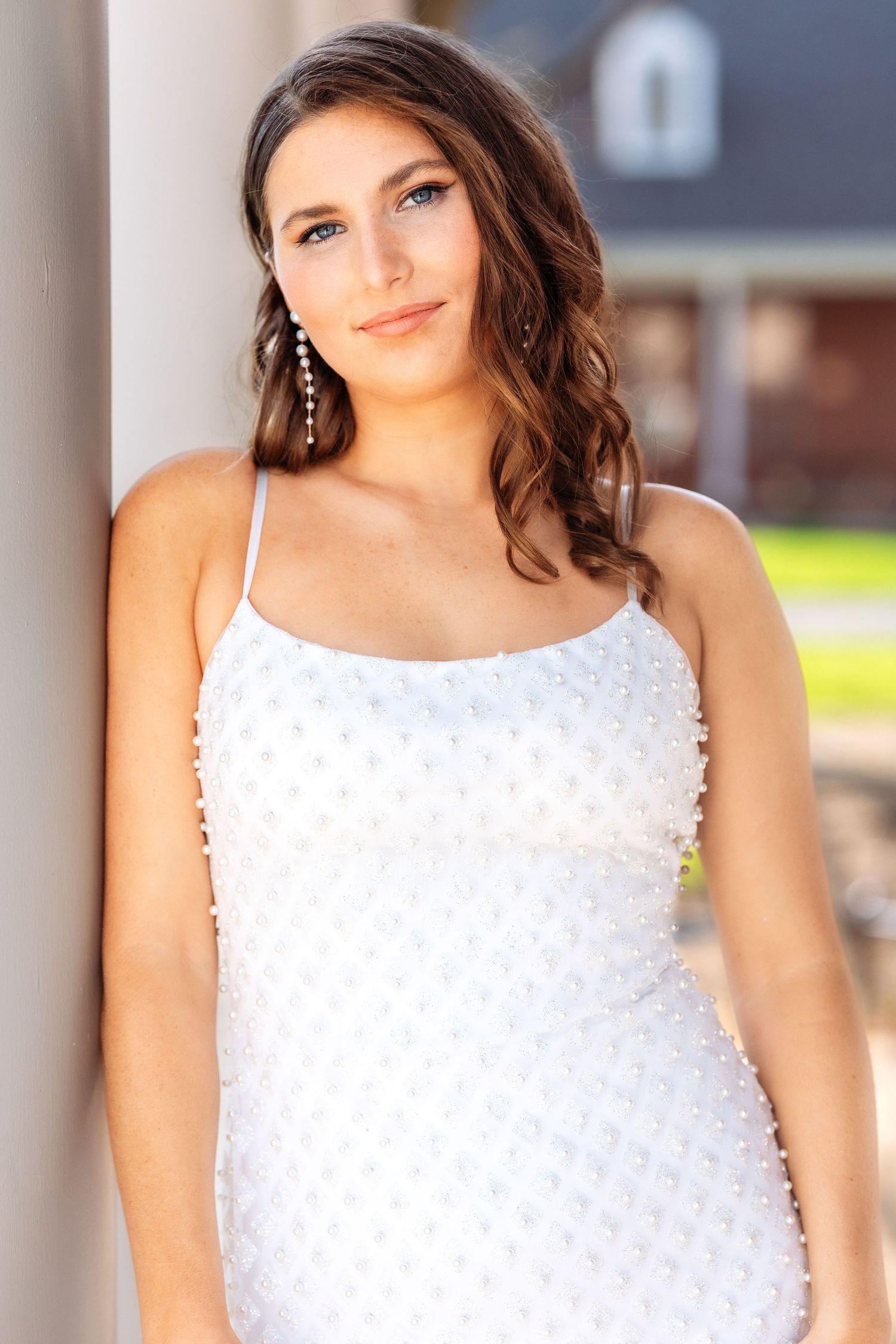 Portrait of someone in a textured white formal dress with delicate spaghetti straps against an outdoor background.