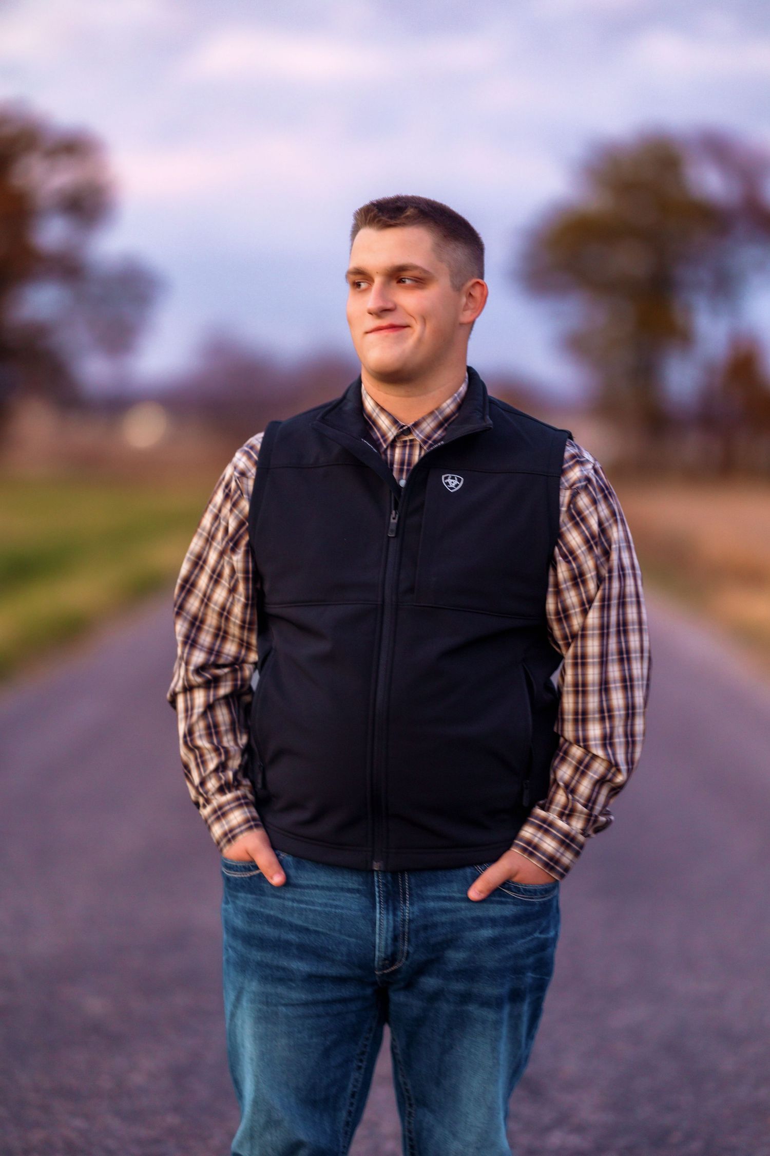 Person in vest and jeans standing on rural road during golden hour.