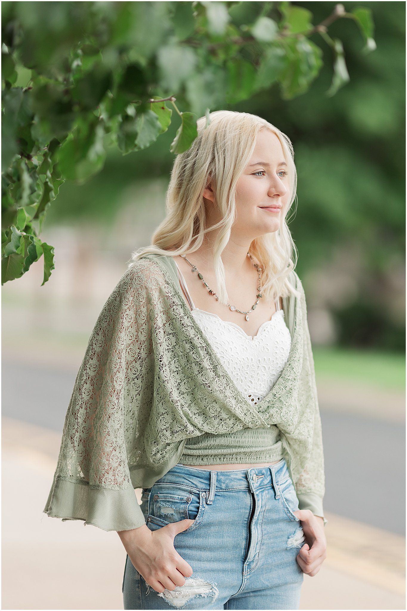 senior girl looking off camera with thumbs in her jeans with leaves in the forground