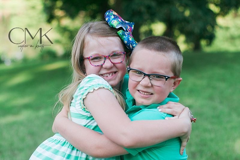 Two children in matching mint green outfits share a warm embrace while smiling outdoors.