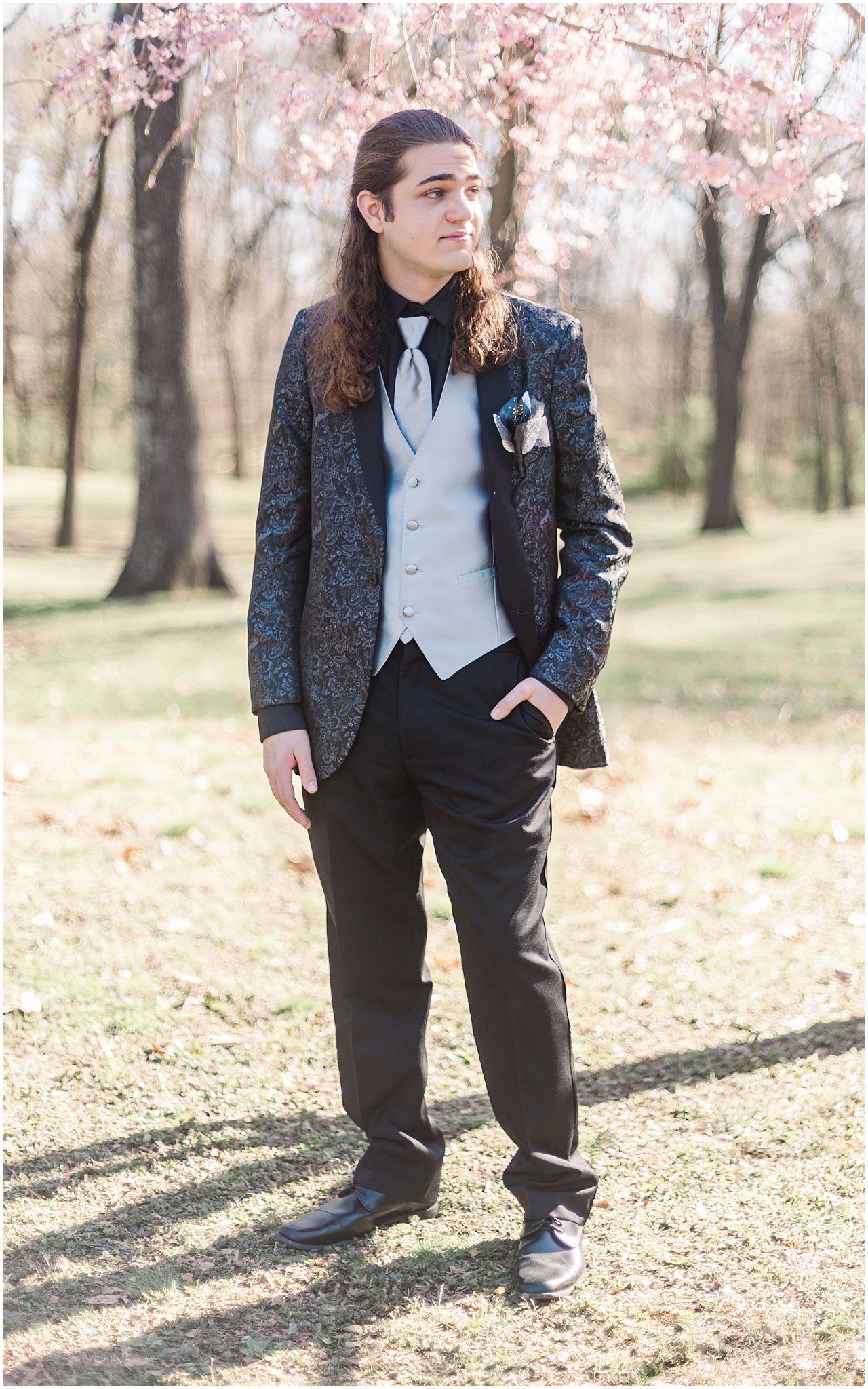 Formal portrait of person in dark patterned suit and vest under cherry blossoms.