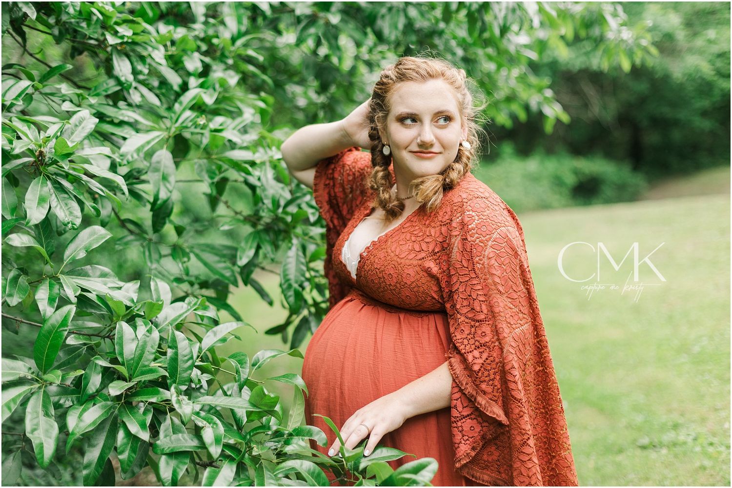 An outdoor maternity portrait featuring a flowing coral dress and natural garden setting.