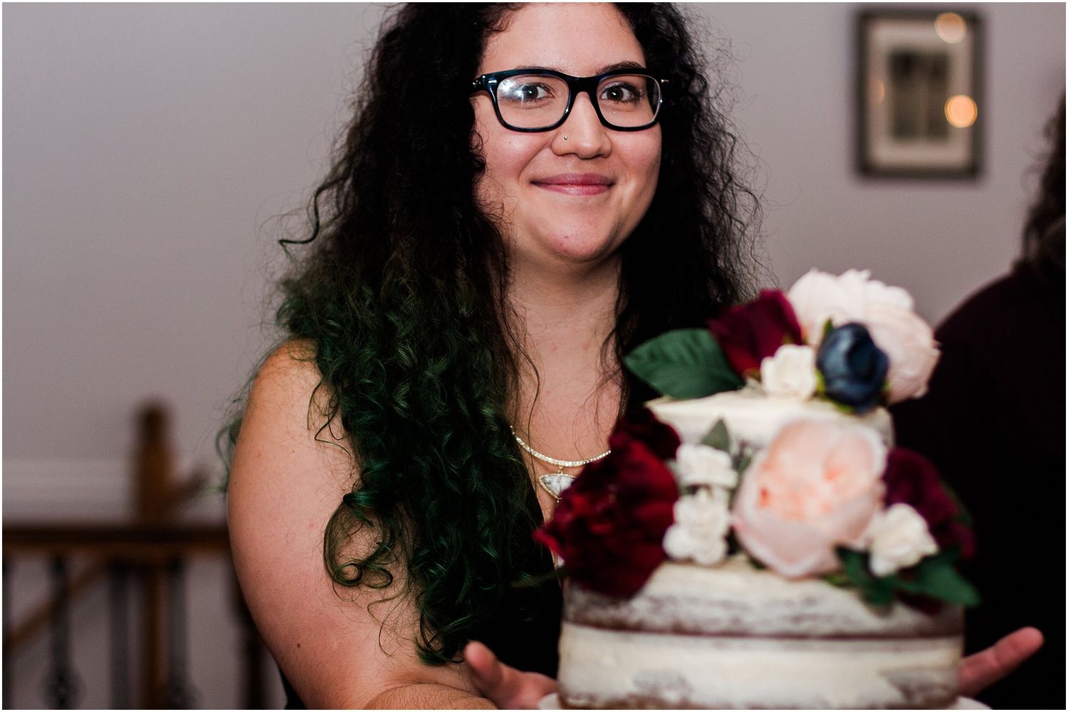 A displayed wedding cake decorated with red and blush colored flowers.