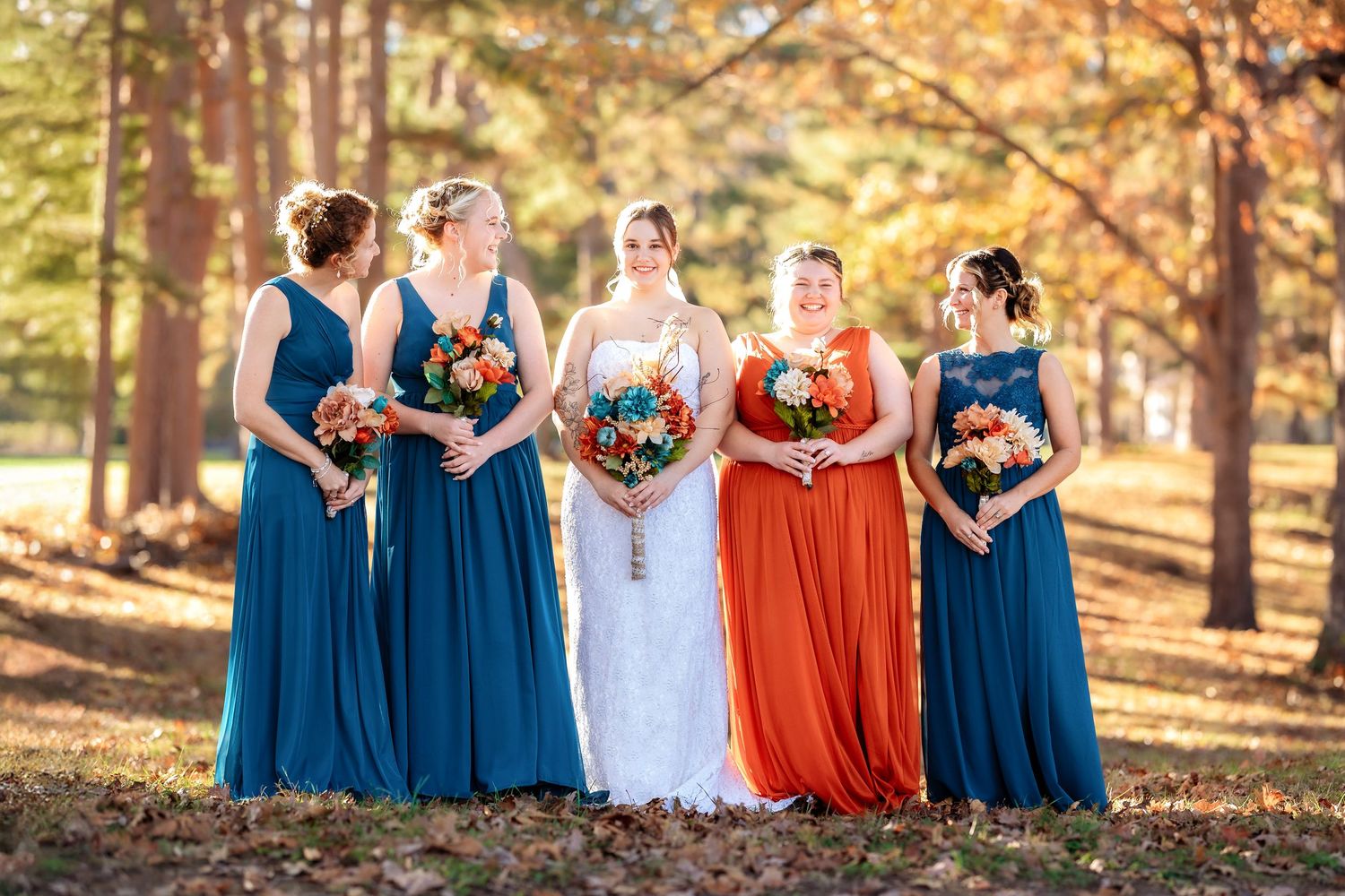 Wedding party in blue and orange dresses posing together in an autumn forest setting.