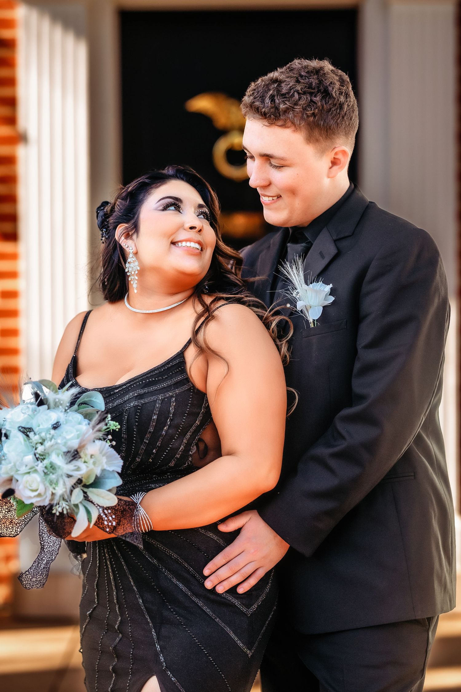 A couple shares an intimate moment in formal attire with the woman wearing black and a light blue floral accessory.