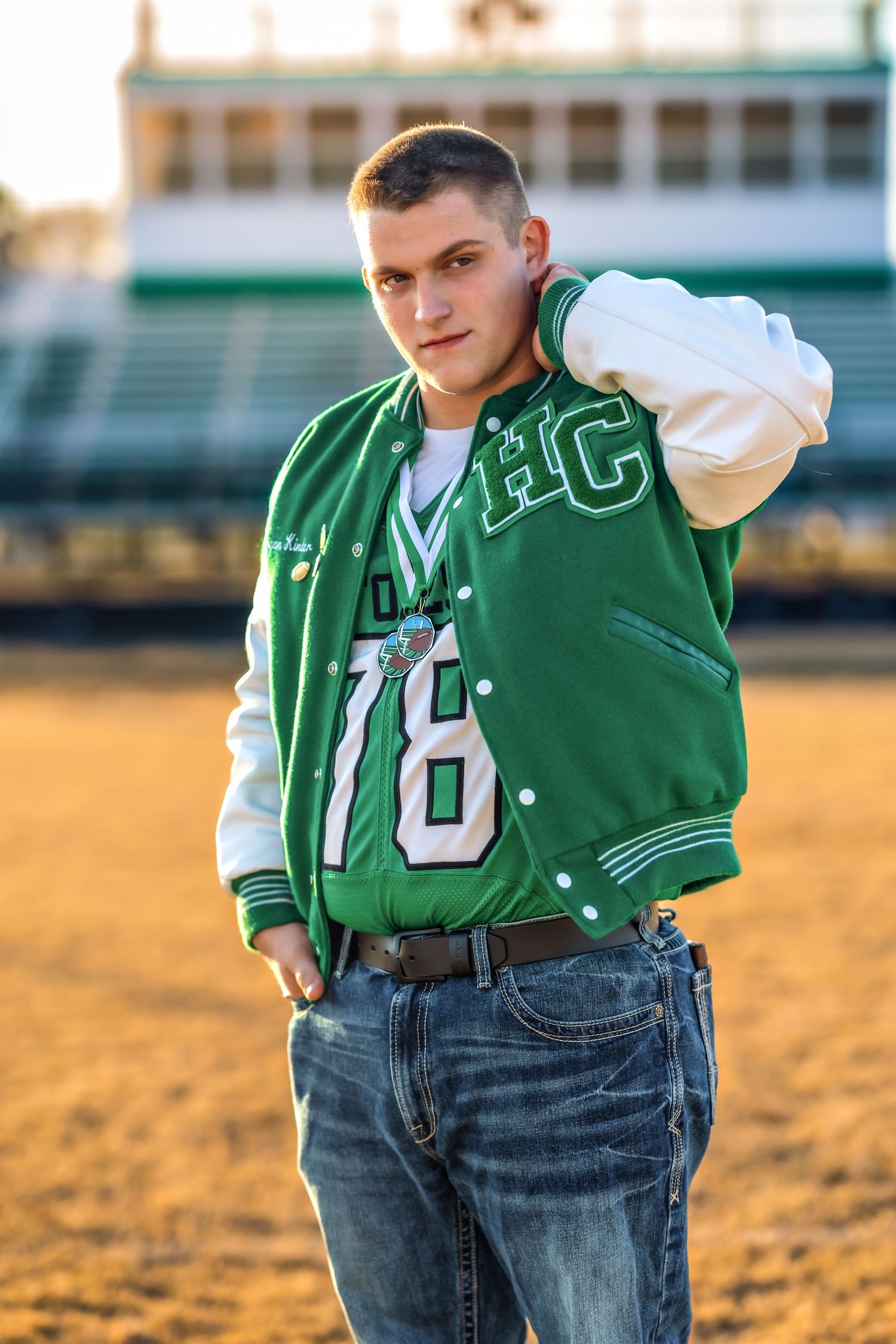 Student in varsity letterman jacket posing outdoors at sunset.