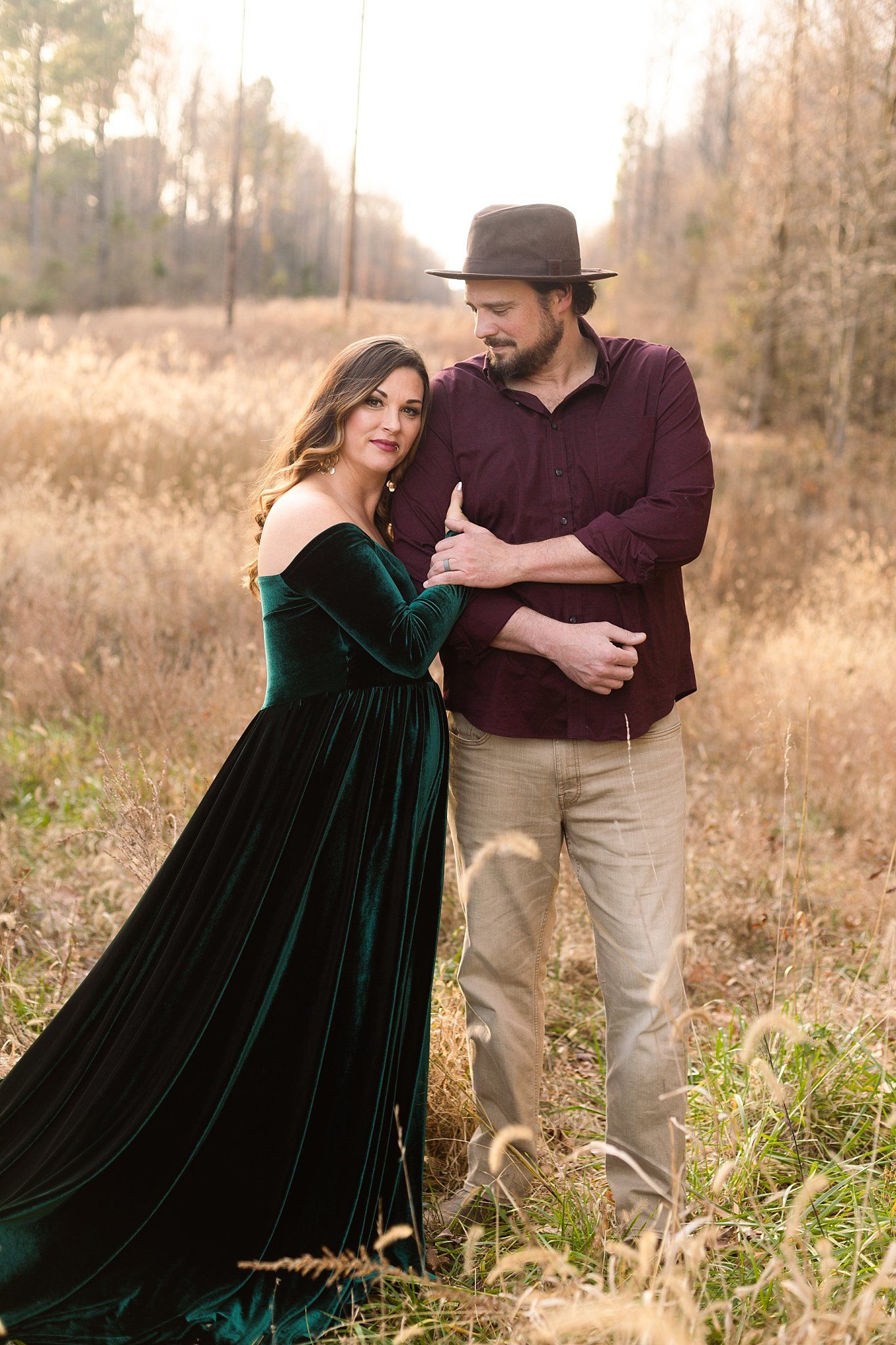 Sweet outdoor maternity photo with couple in emerald velvet gown and burgundy button-down.