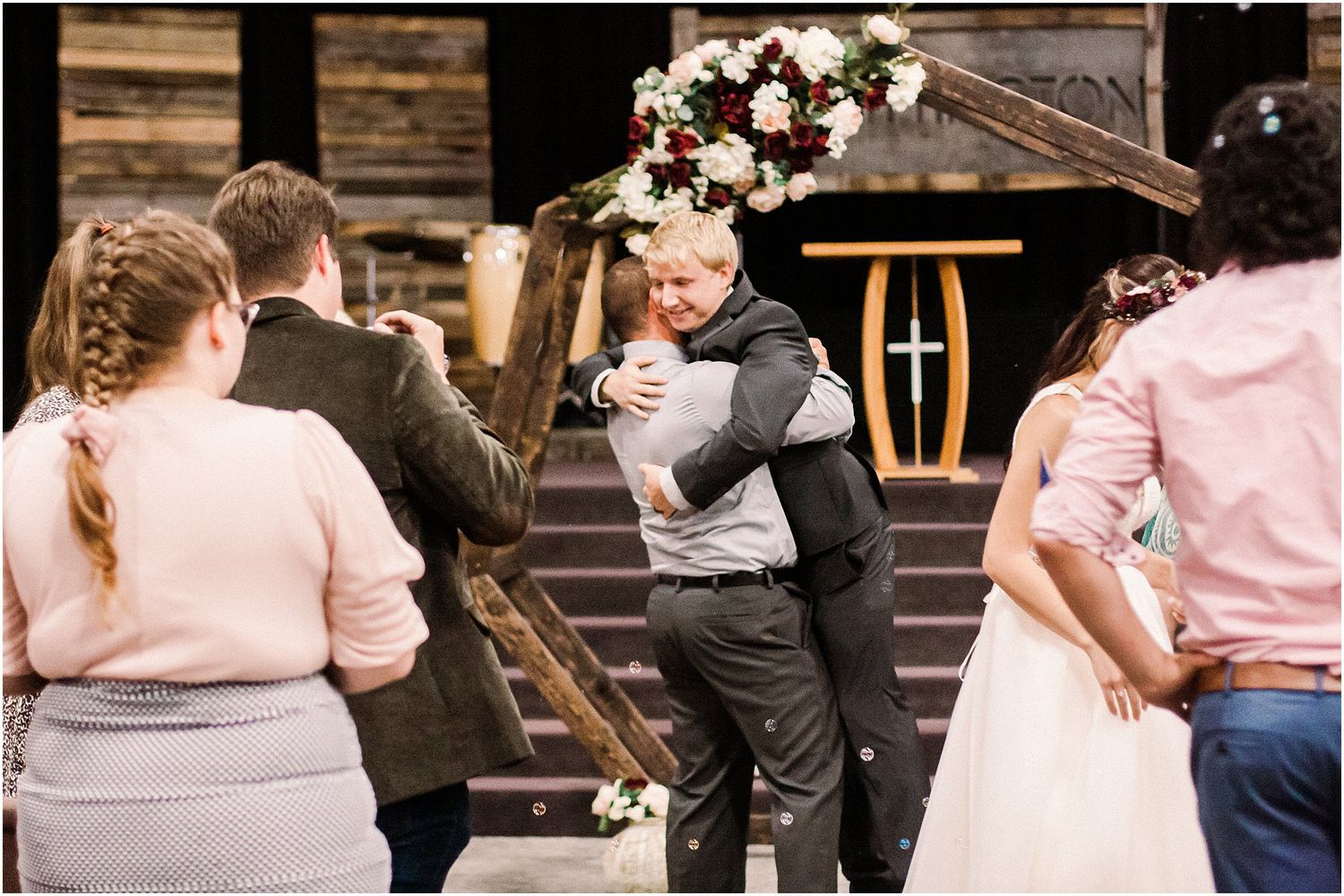 Wedding guests gather around a rustic wooden arch during post-ceremony celebrations.