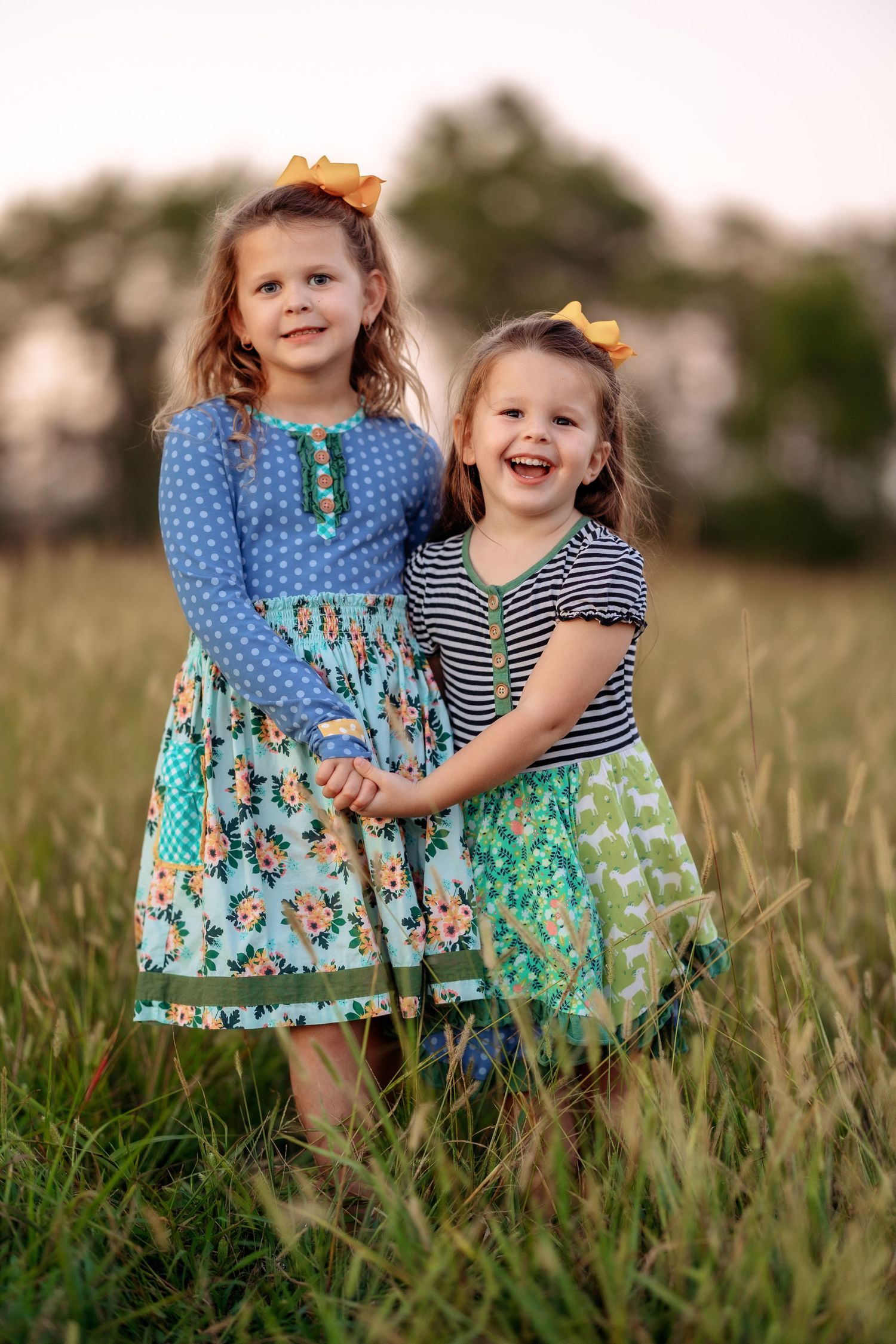 Two young children in matching floral dresses playing together in a grassy field at sunset.