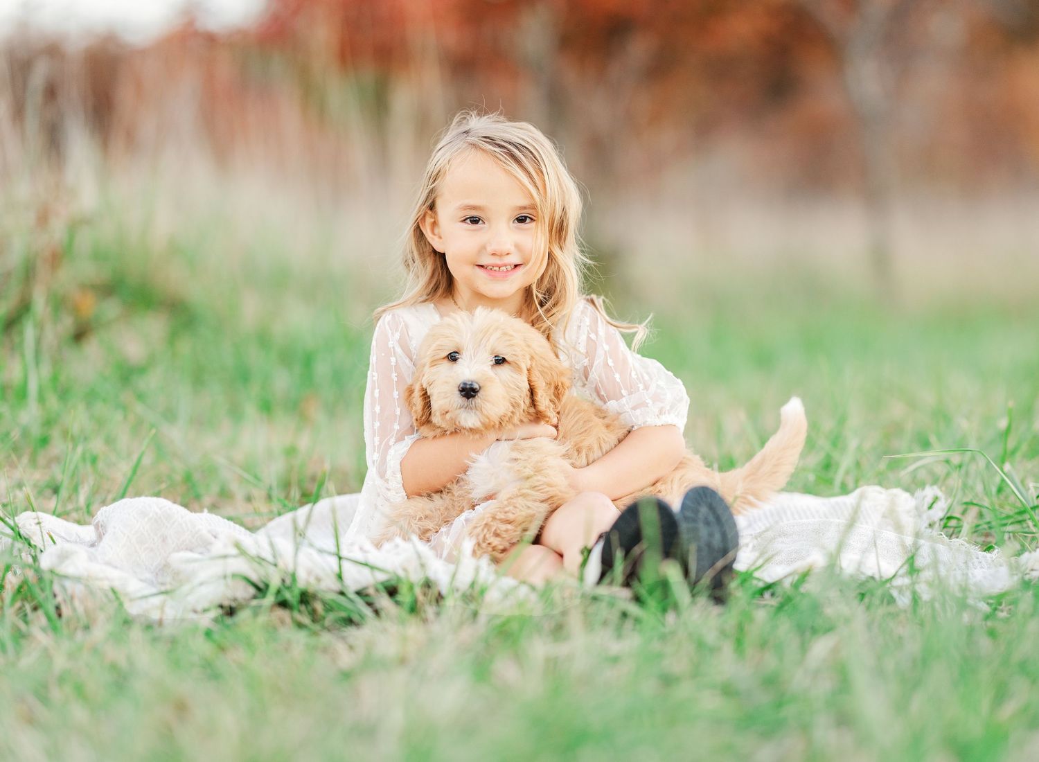 Golden retriever puppy plays with family on blanket in grassy field.