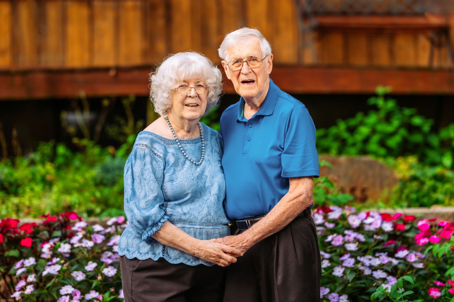 Elderly couple shares affectionate moments in a garden setting with colorful flowers.