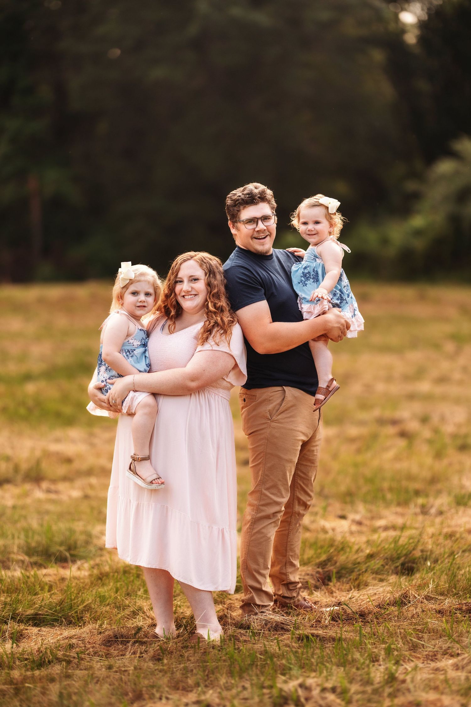 Family group poses together in field during golden hour photoshoot.