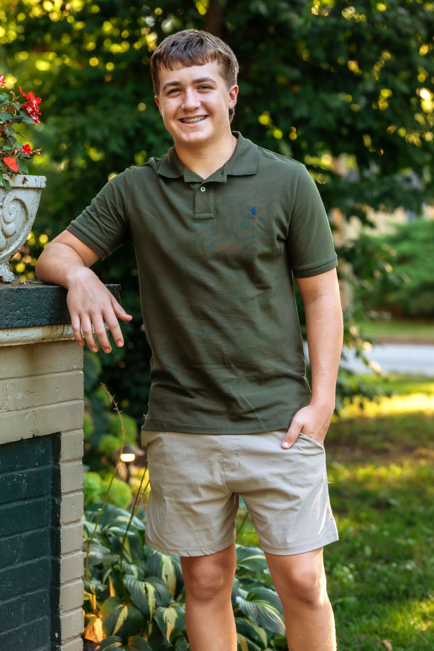 Person in olive green polo and khaki shorts poses casually in a garden setting.
