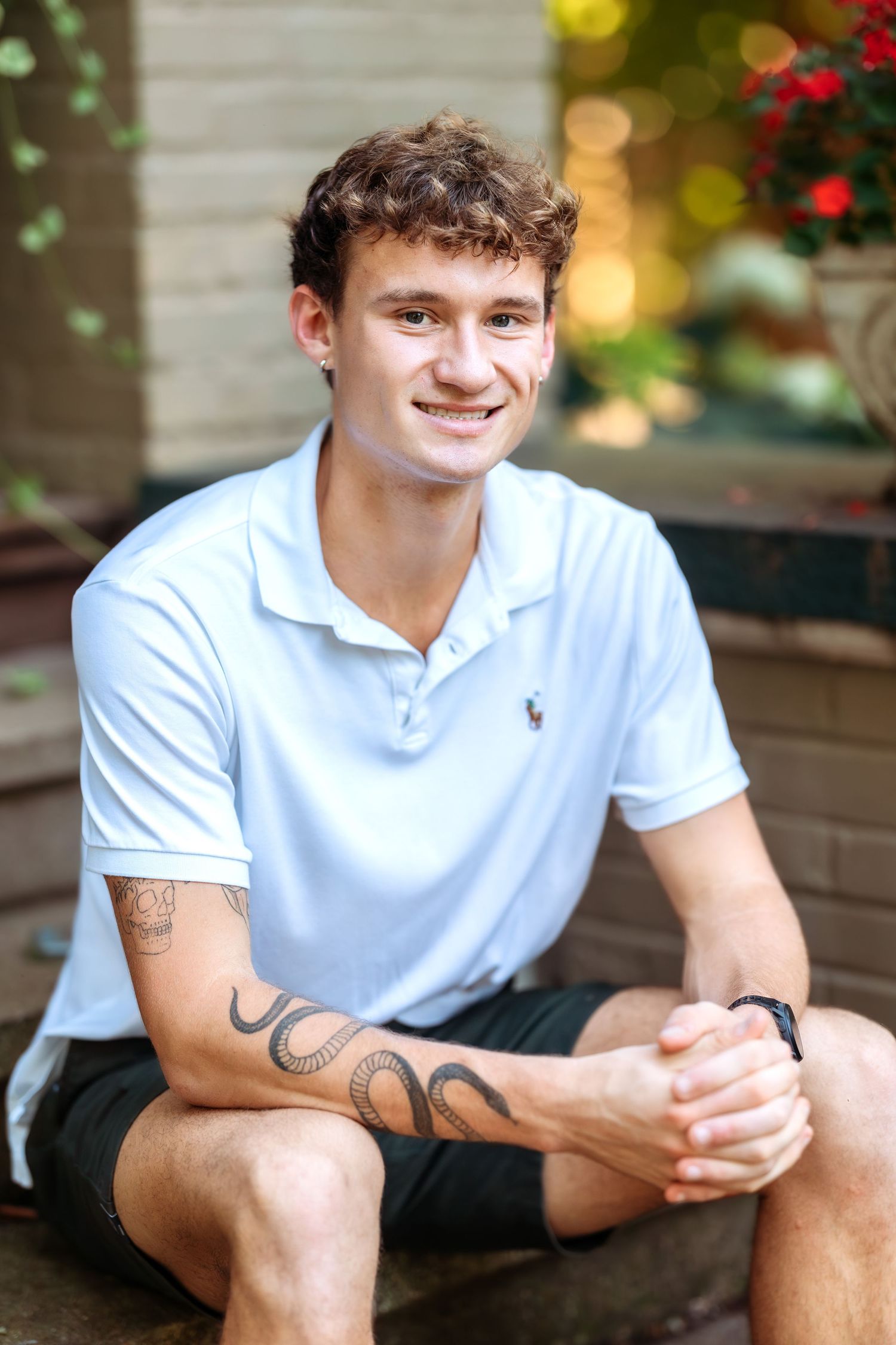Person in white polo shirt sits casually outdoors showing tattoo on arm.