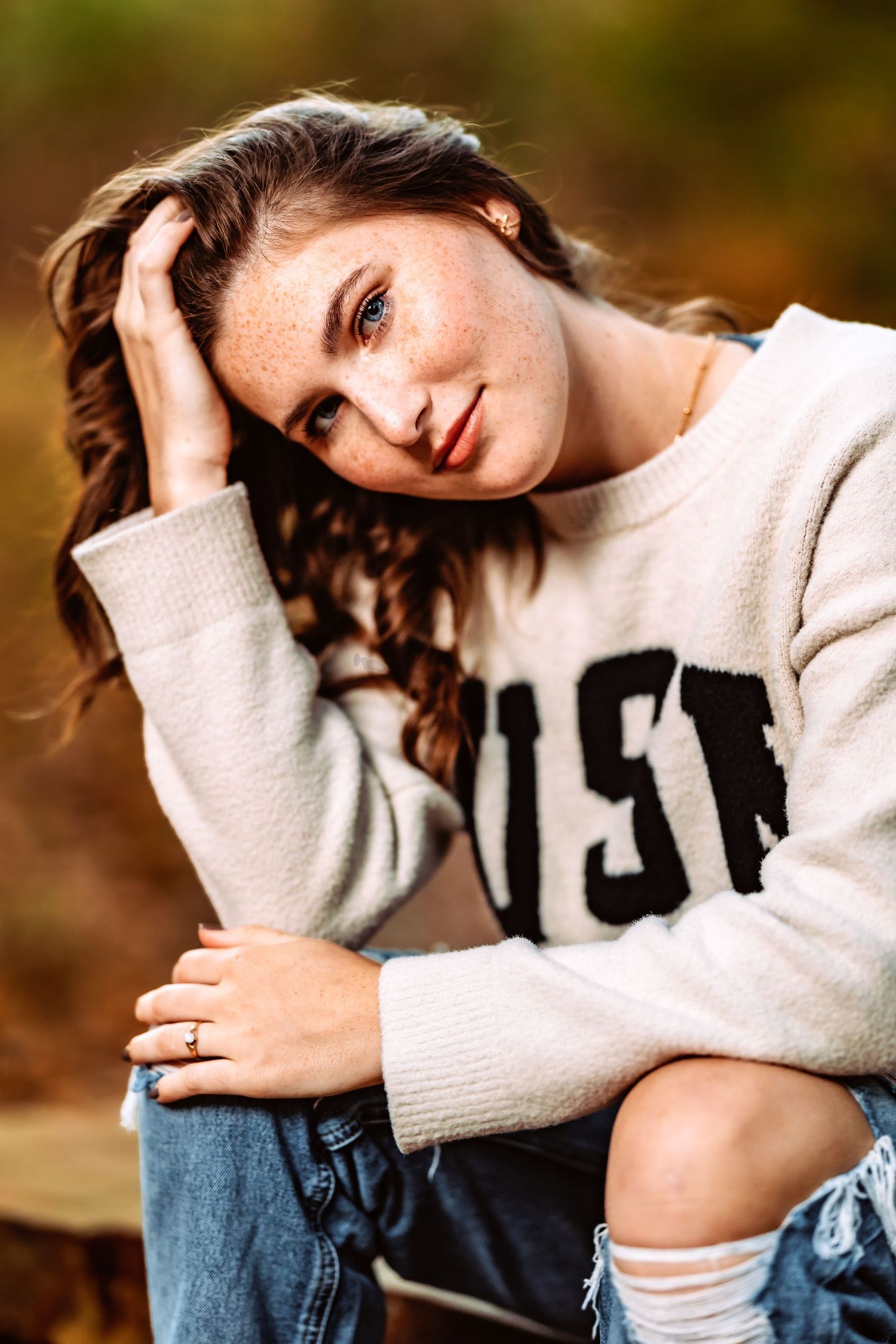 Casual autumn portrait featuring a cream sweater and distressed jeans against a warm blurred background.