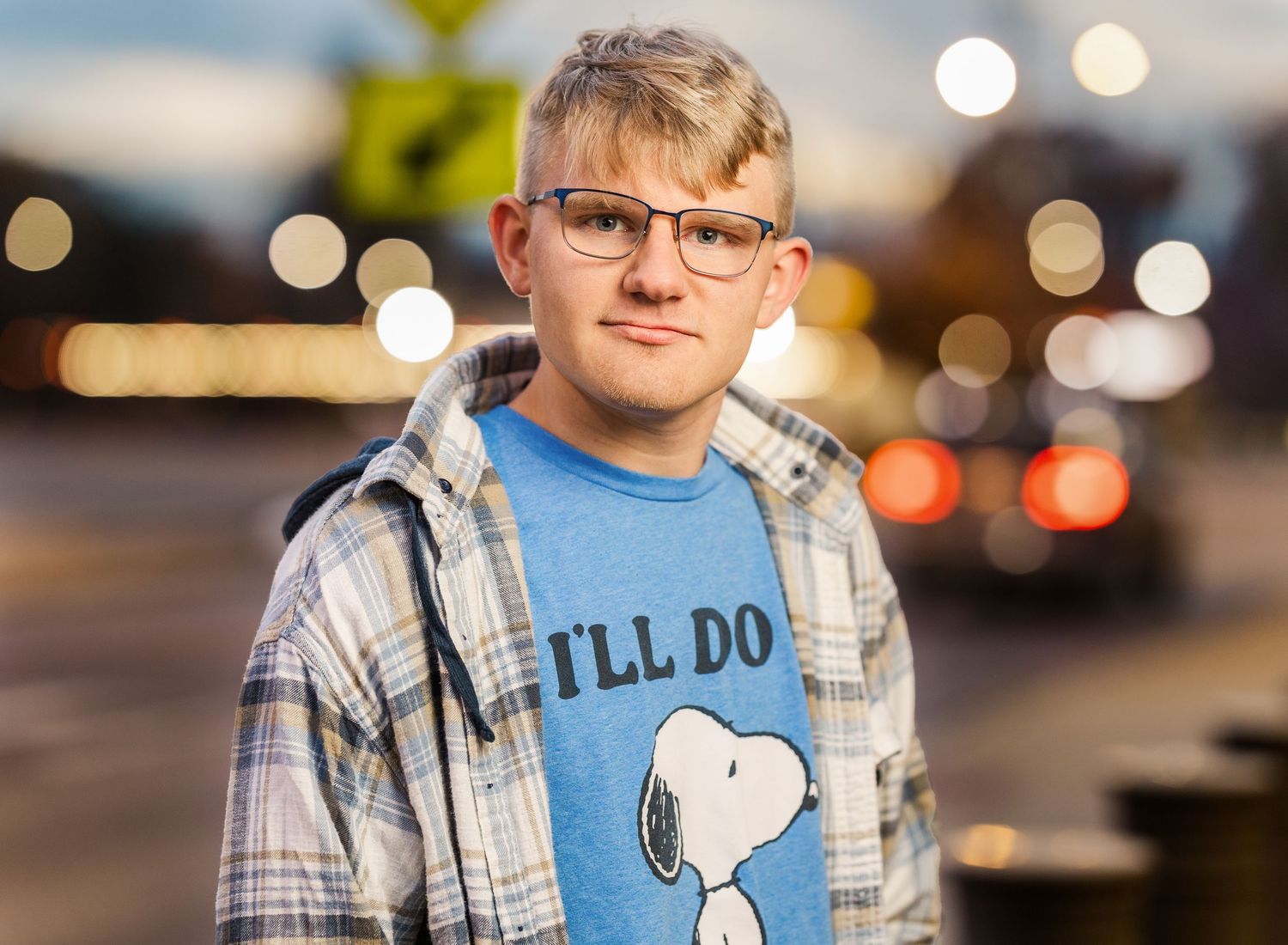 Person wearing a Snoopy graphic t-shirt and plaid shirt in an outdoor setting with bokeh lights.