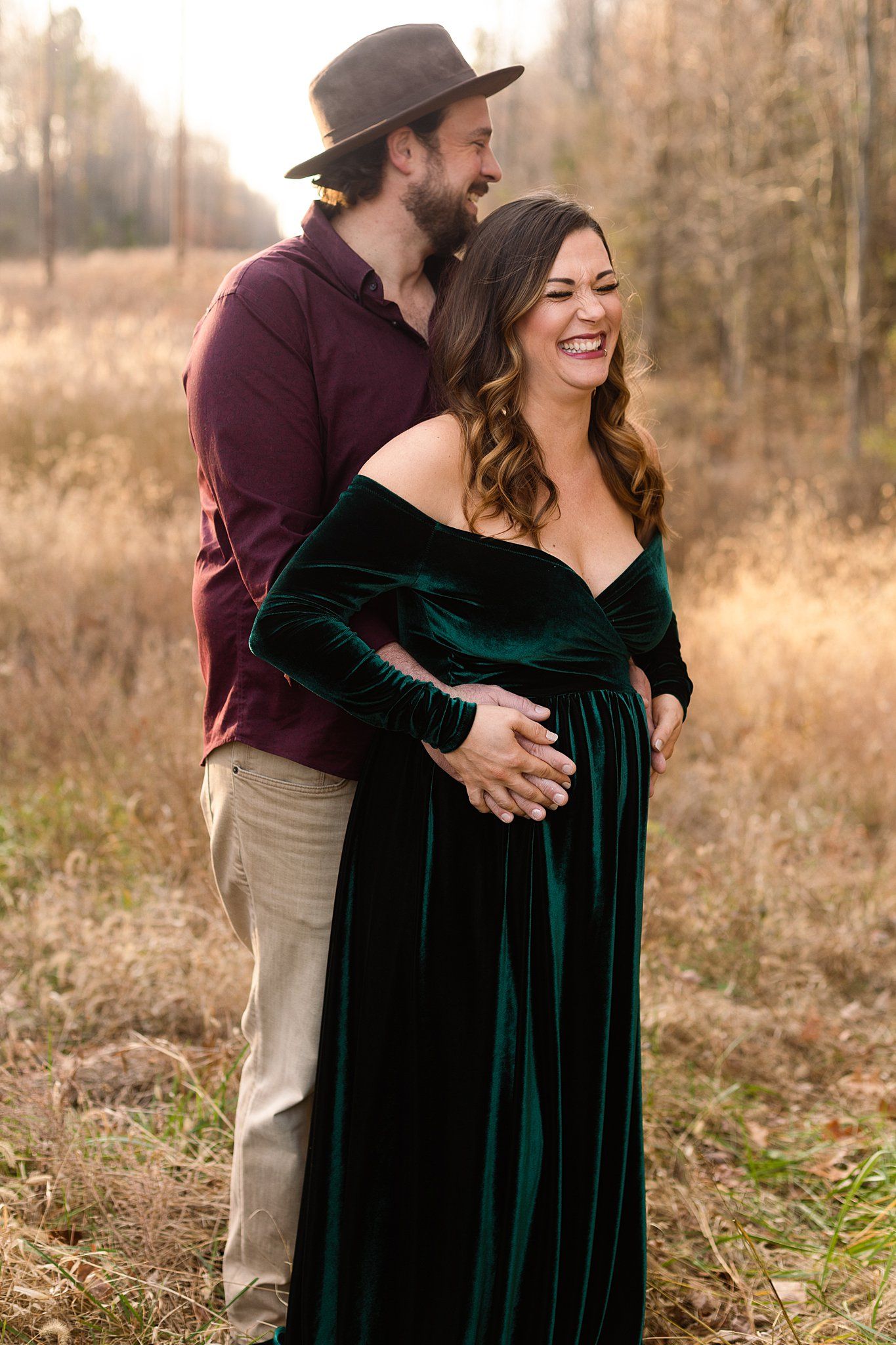 Maternity photoshoot featuring couple in emerald velvet dress and burgundy shirt outdoors.