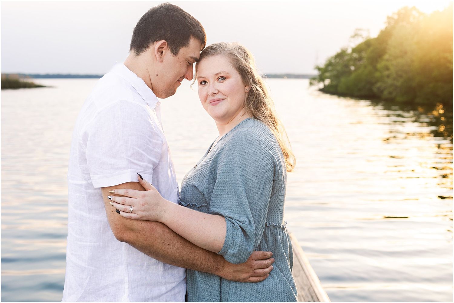 Intimate moment captured at sunset with couple embracing on dock by the water.