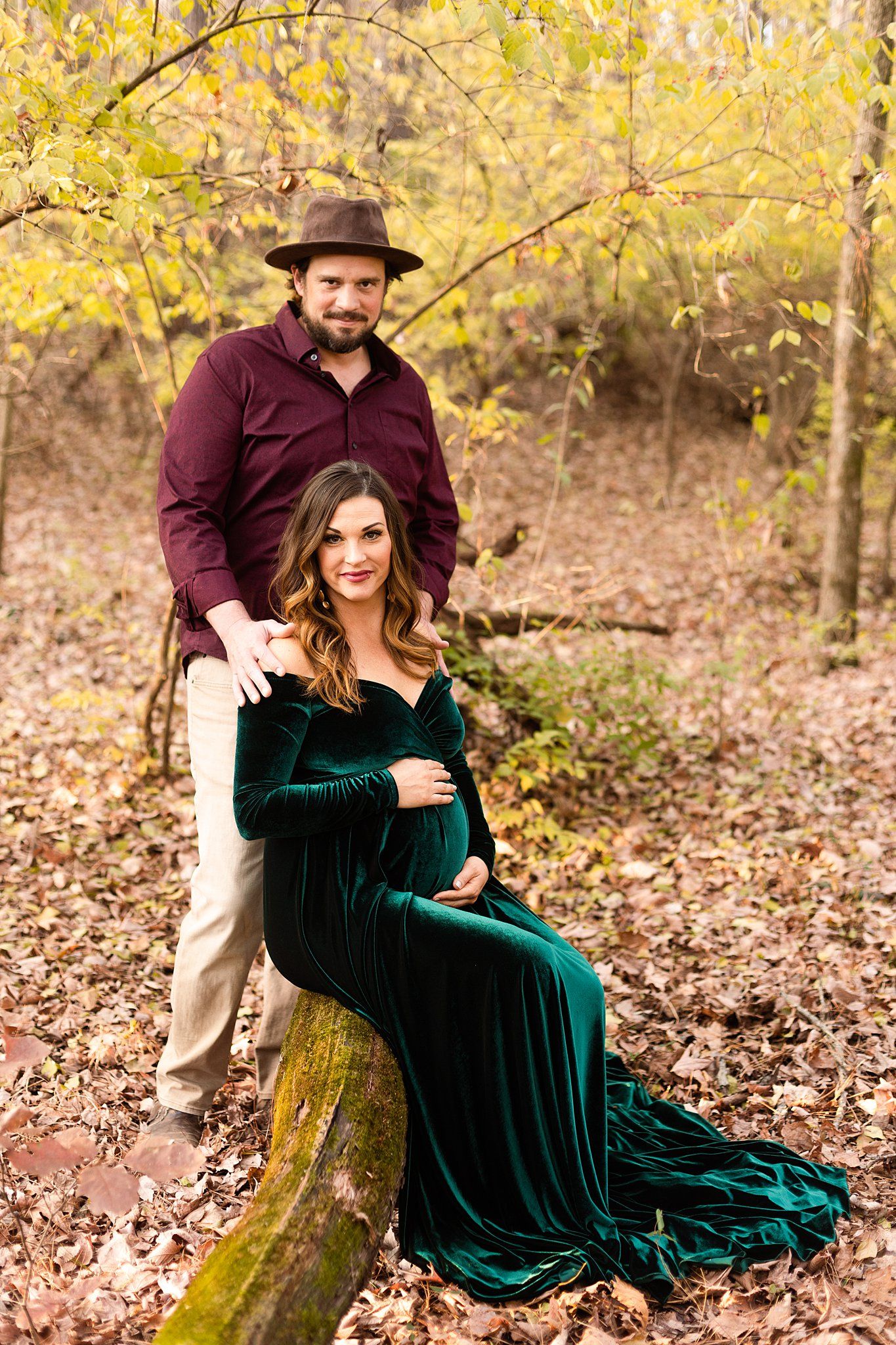 Autumn forest maternity photo with couple by moss-covered log.