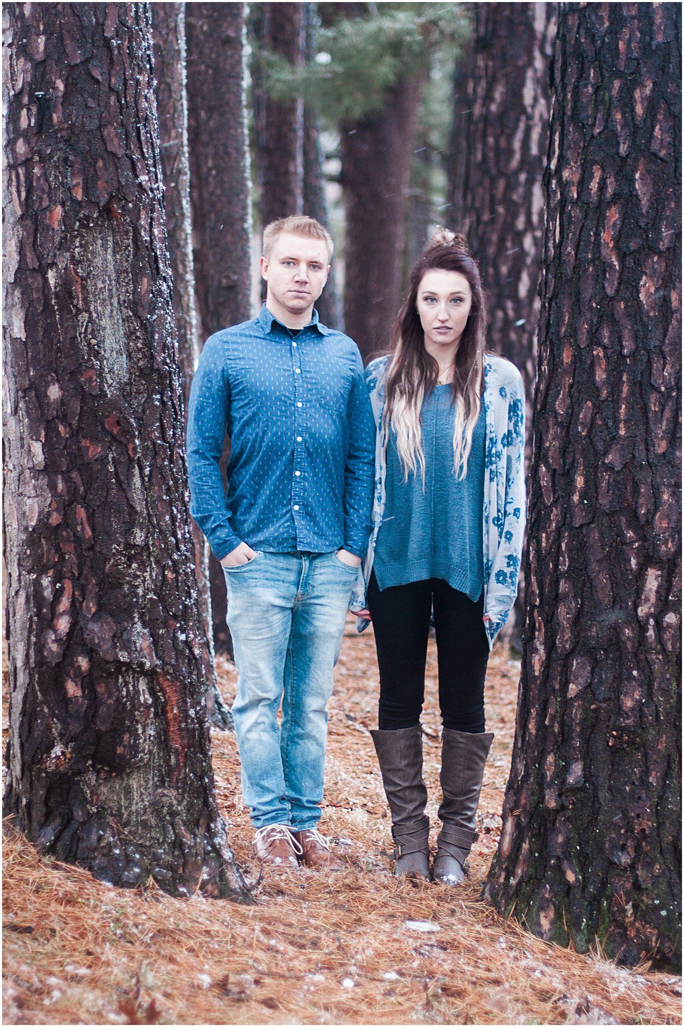 Couple standing between pine trees in a forest wearing coordinated blue outfits.
