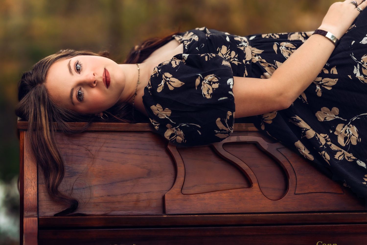 Elegant portrait session featuring a black floral dress against a dark wooden bench in a studio setting.