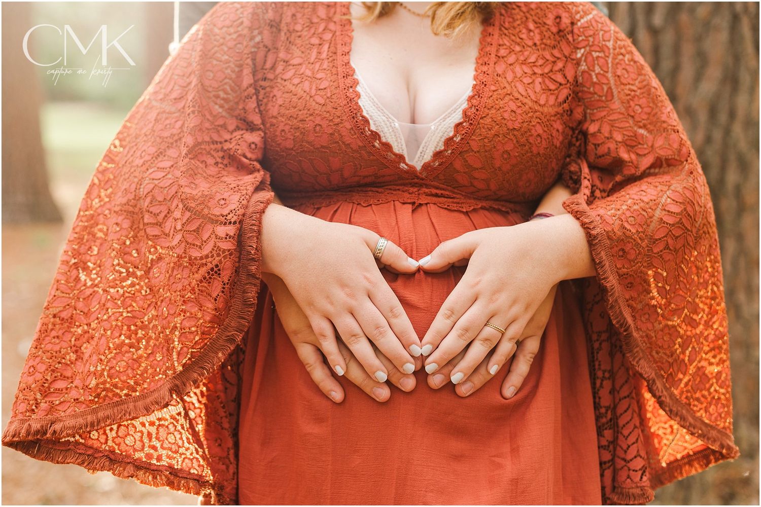 Close-up shot of hands cradling a pregnant belly in a rust-colored lace dress.