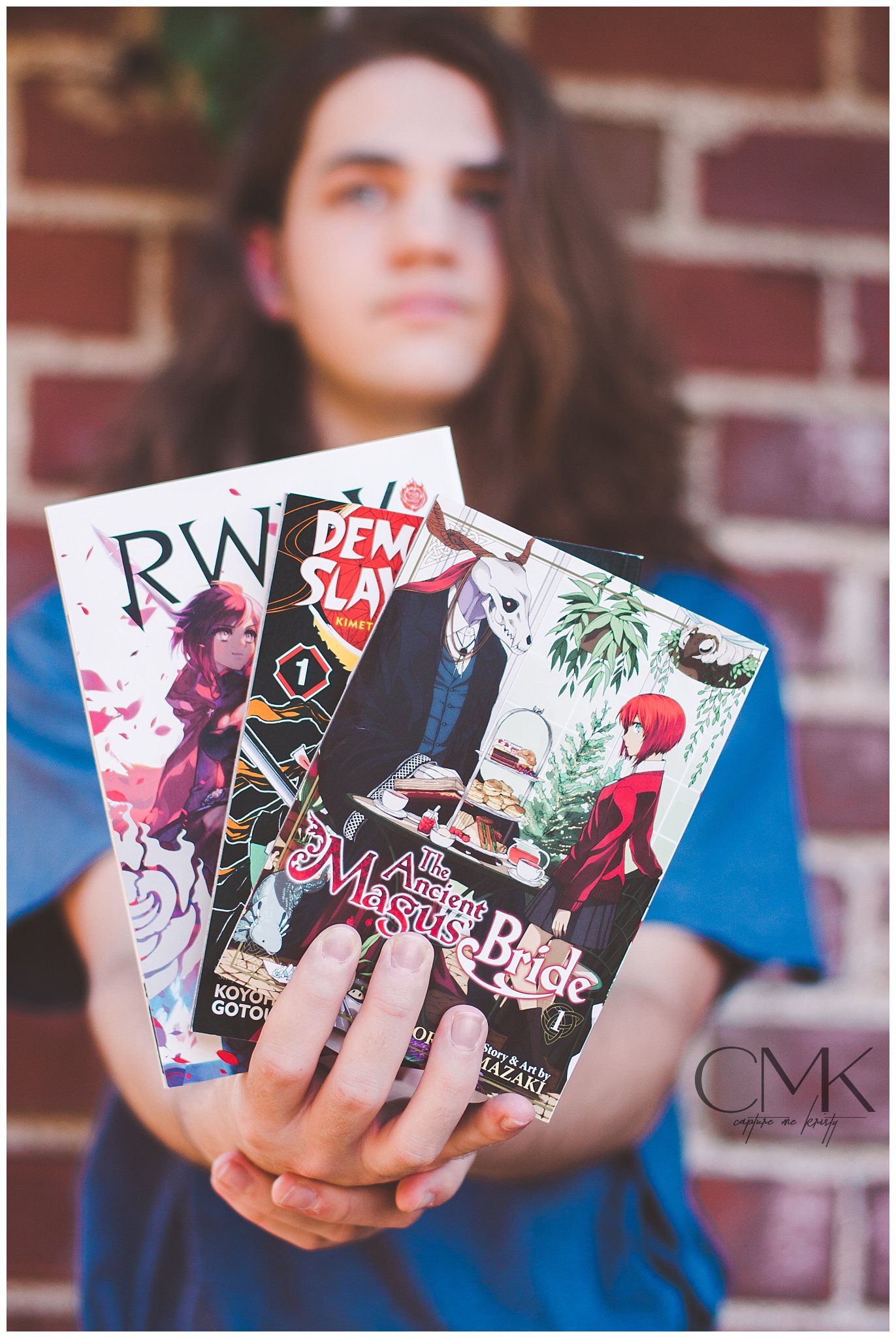 Person displaying collection of manga books in front of brick wall.