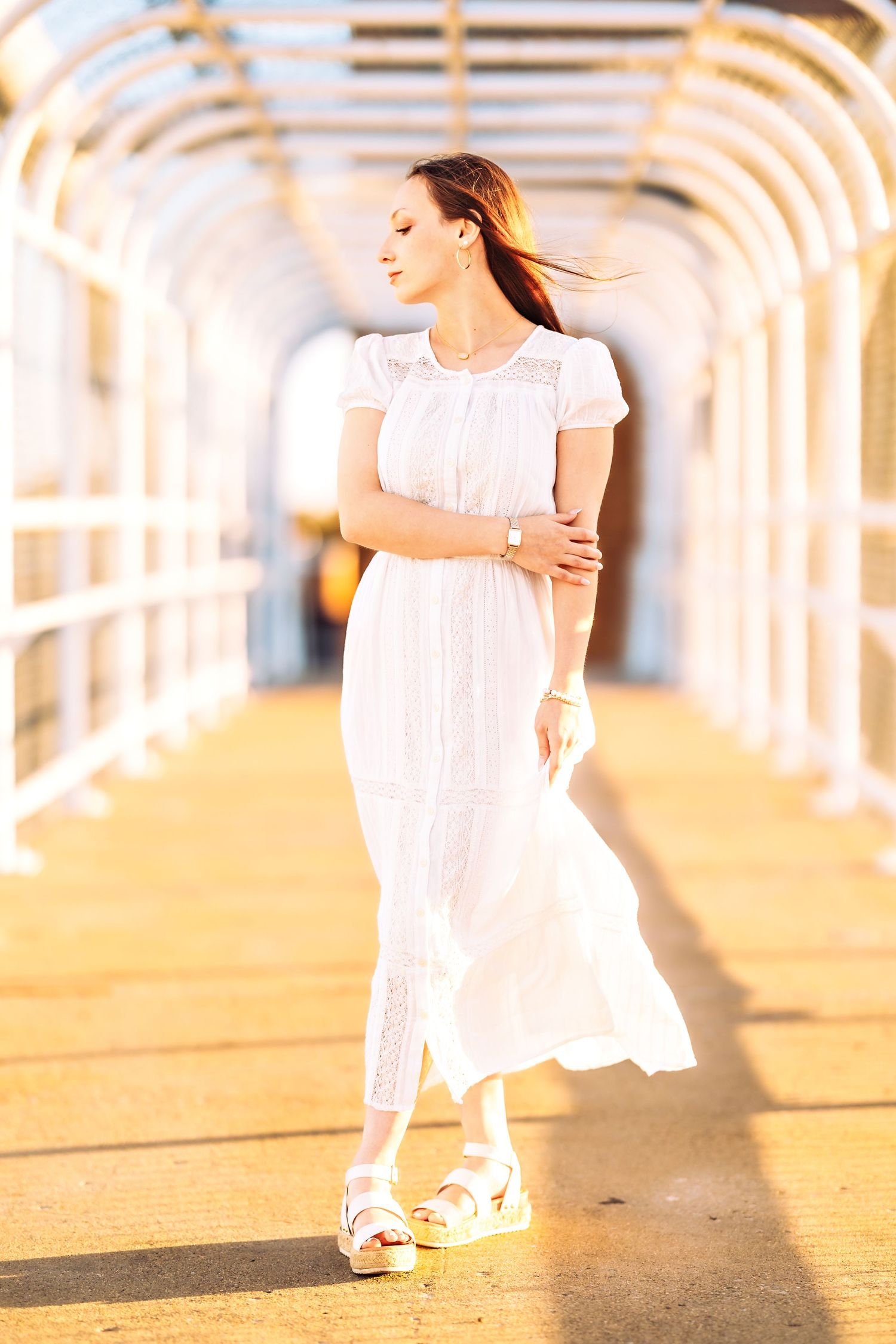 Person in white flowing dress twirls in sunlit archway corridor.