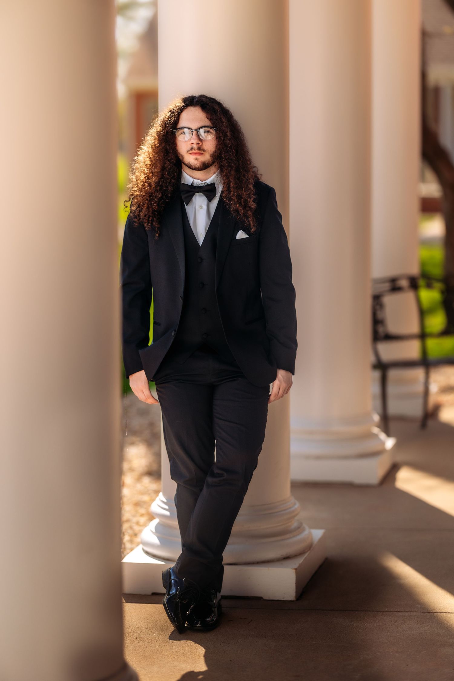 A figure in a black suit poses between elegant white columns in a series of professional portraits.