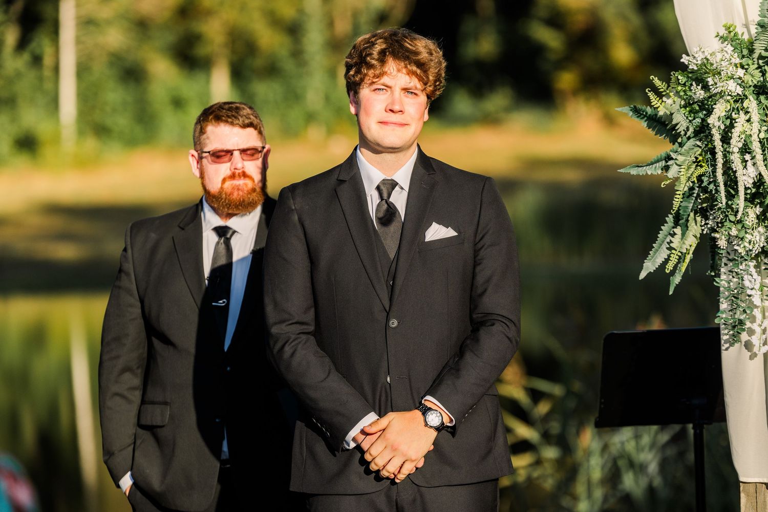 Two groomsmen stand at attention during an outdoor wedding ceremony.