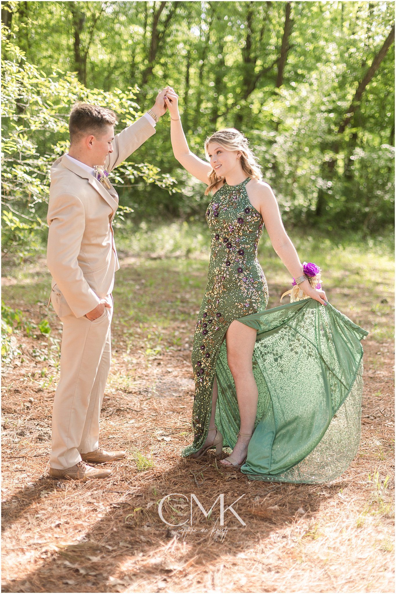 Dancing couple in formal wear twirl in a sunlit forest with flowing green sequined dress.