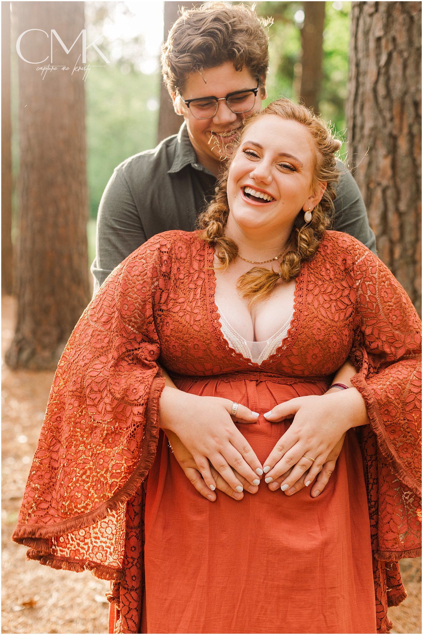A romantic outdoor photoshoot featuring a couple embracing in front of tall trees.